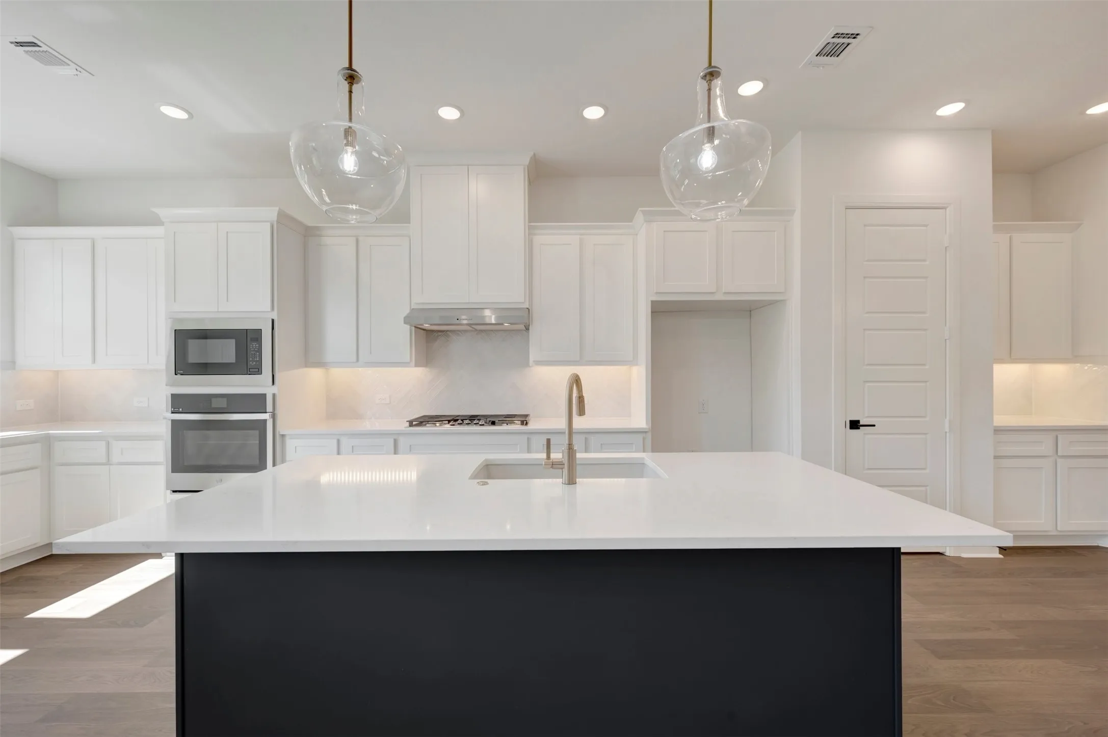Spacious kitchen featuring white cabinetry, a large kitchen island with a light-colored countertop, integrated stainless steel appliances, and wood-finish flooring