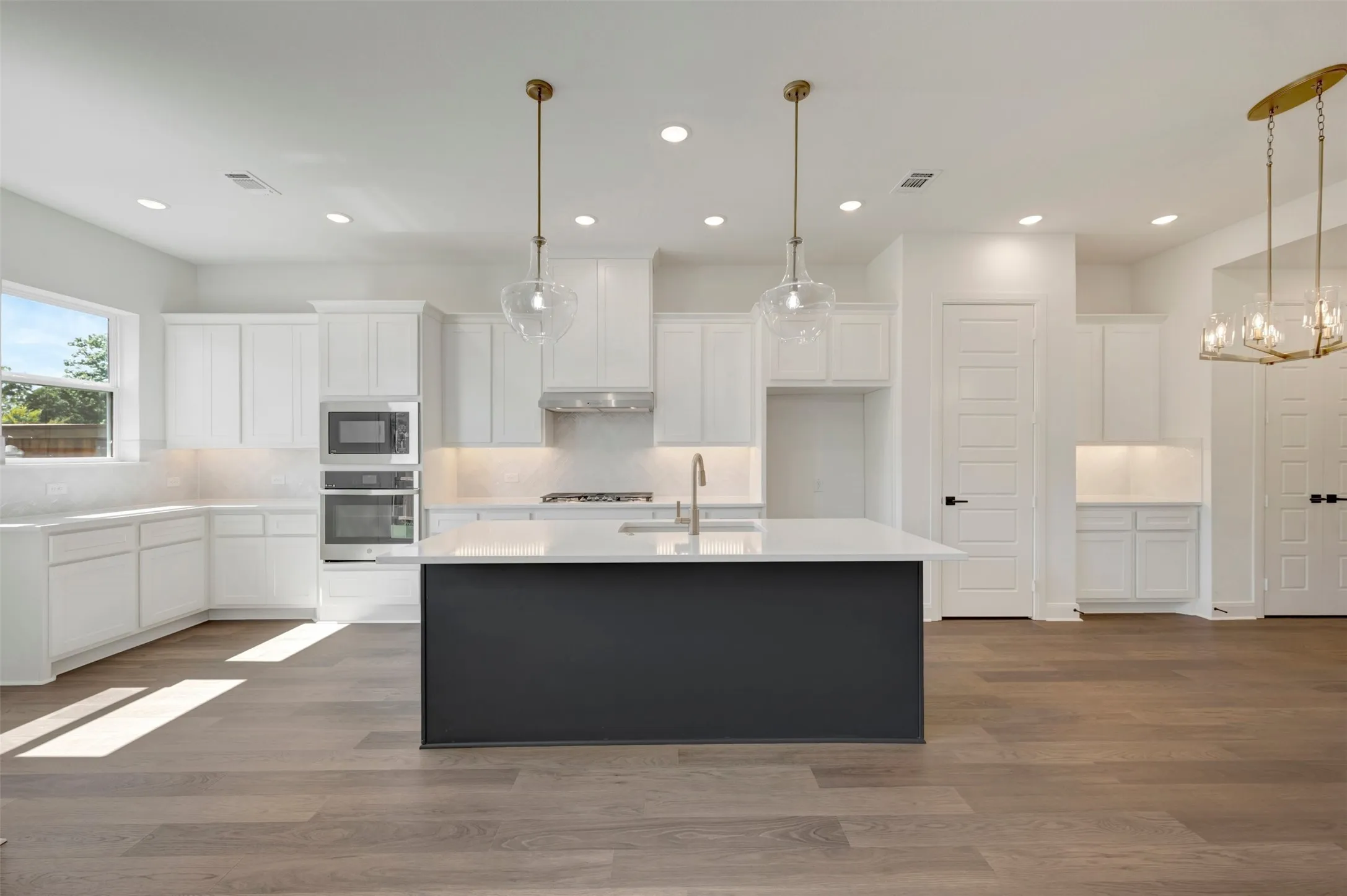 Spacious kitchen featuring an expansive center island, integrated stainless steel appliances, white cabinetry, undermount sink, and wood-finish flooring