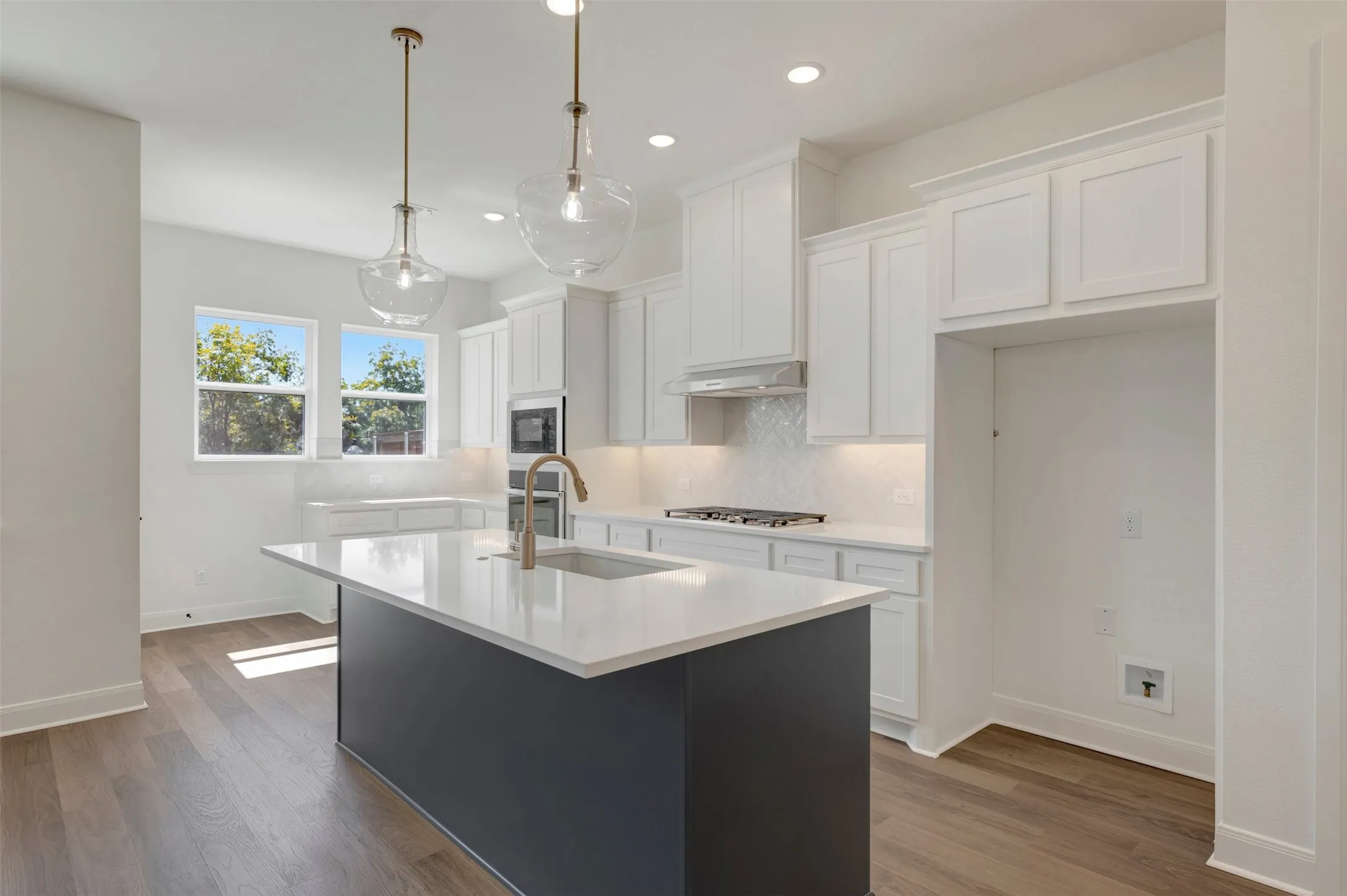 Kitchen featuring white cabinetry, a dark-toned island with a white countertop, stainless steel appliances, and wood-finish flooring
