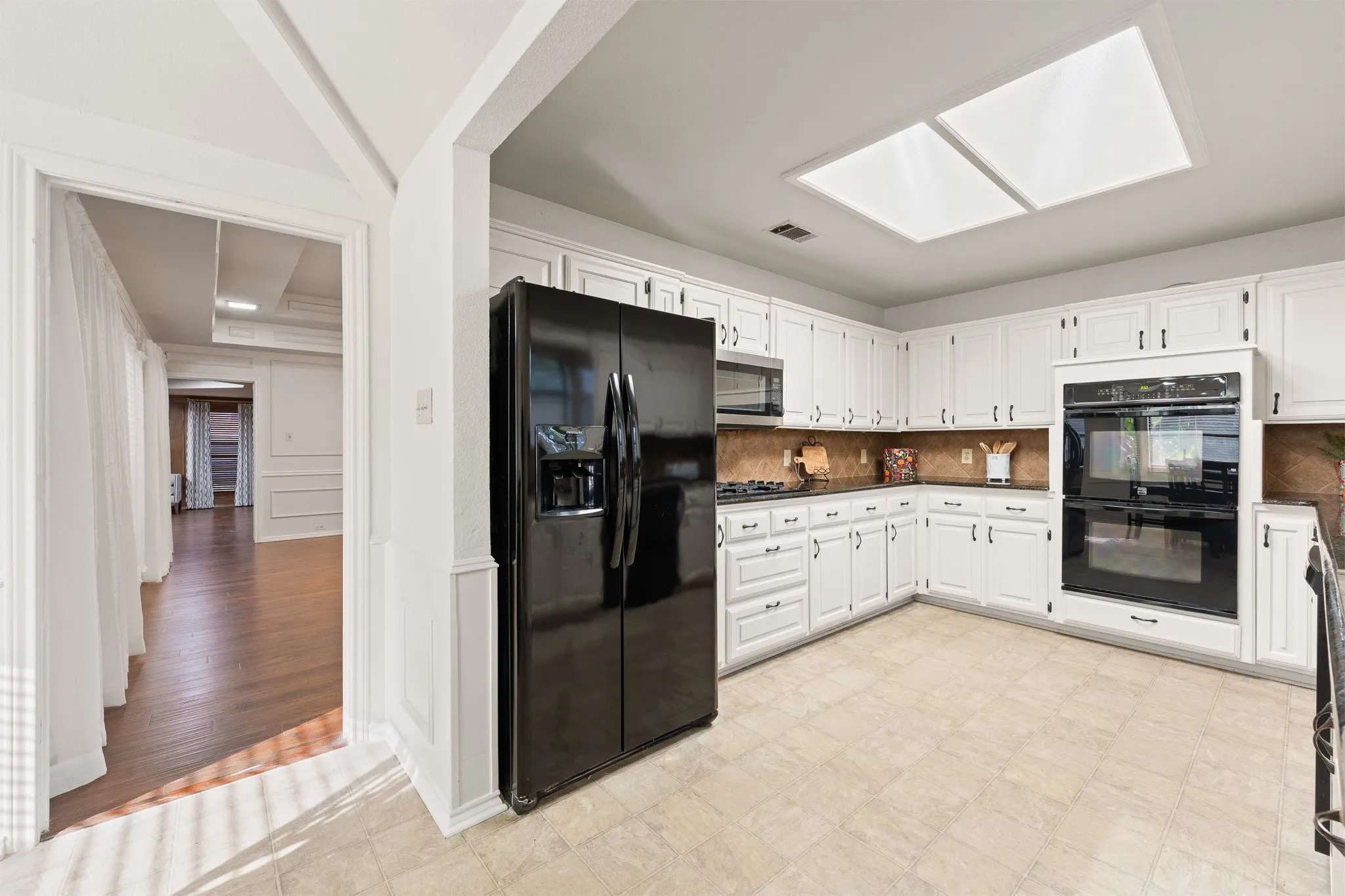 Kitchen featuring white cabinetry, a skylight, tile flooring, and integrated double ovens
