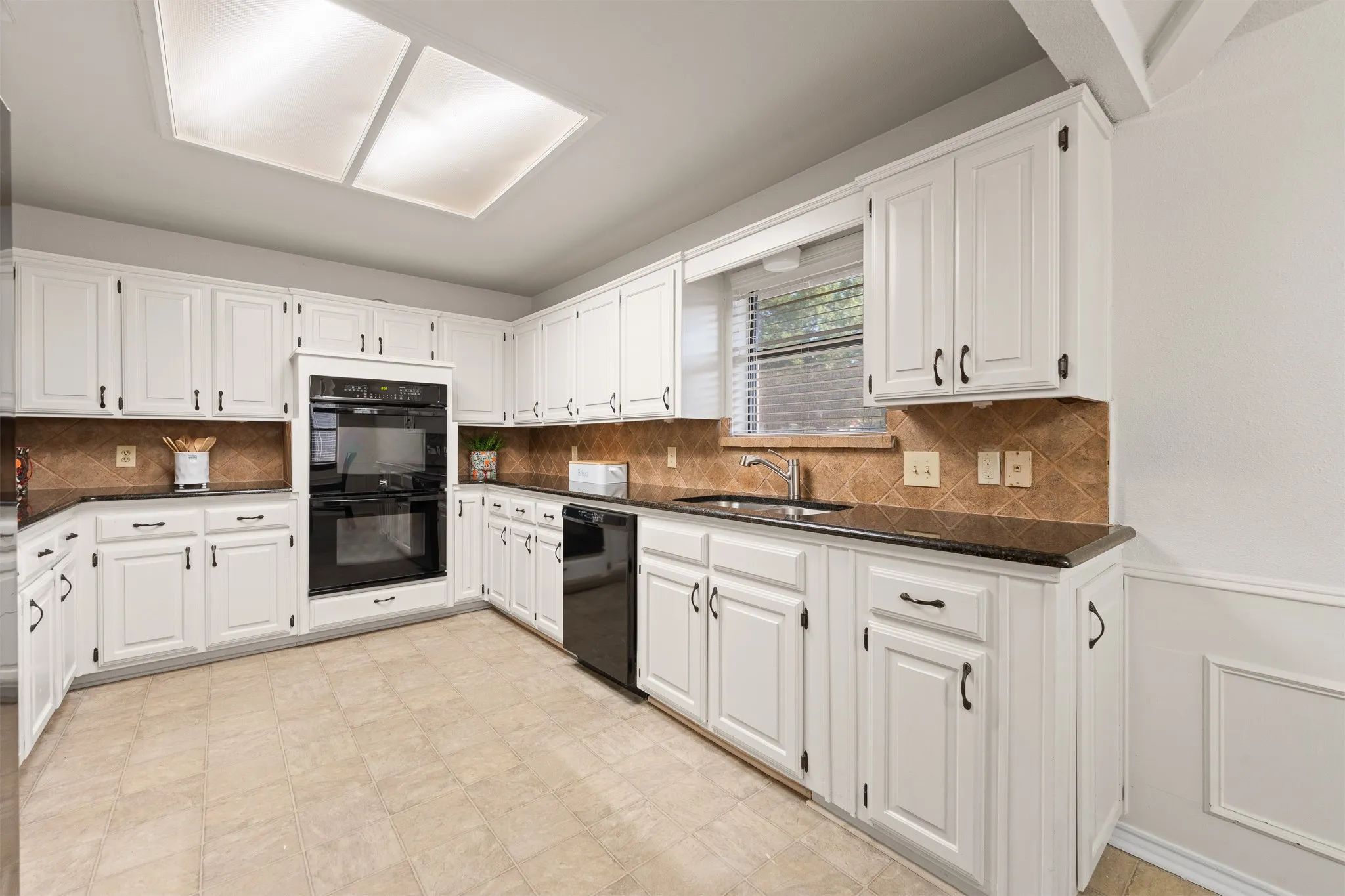 White cabinetry with dark hardware, brown tile backsplash, dark countertops, and tile flooring