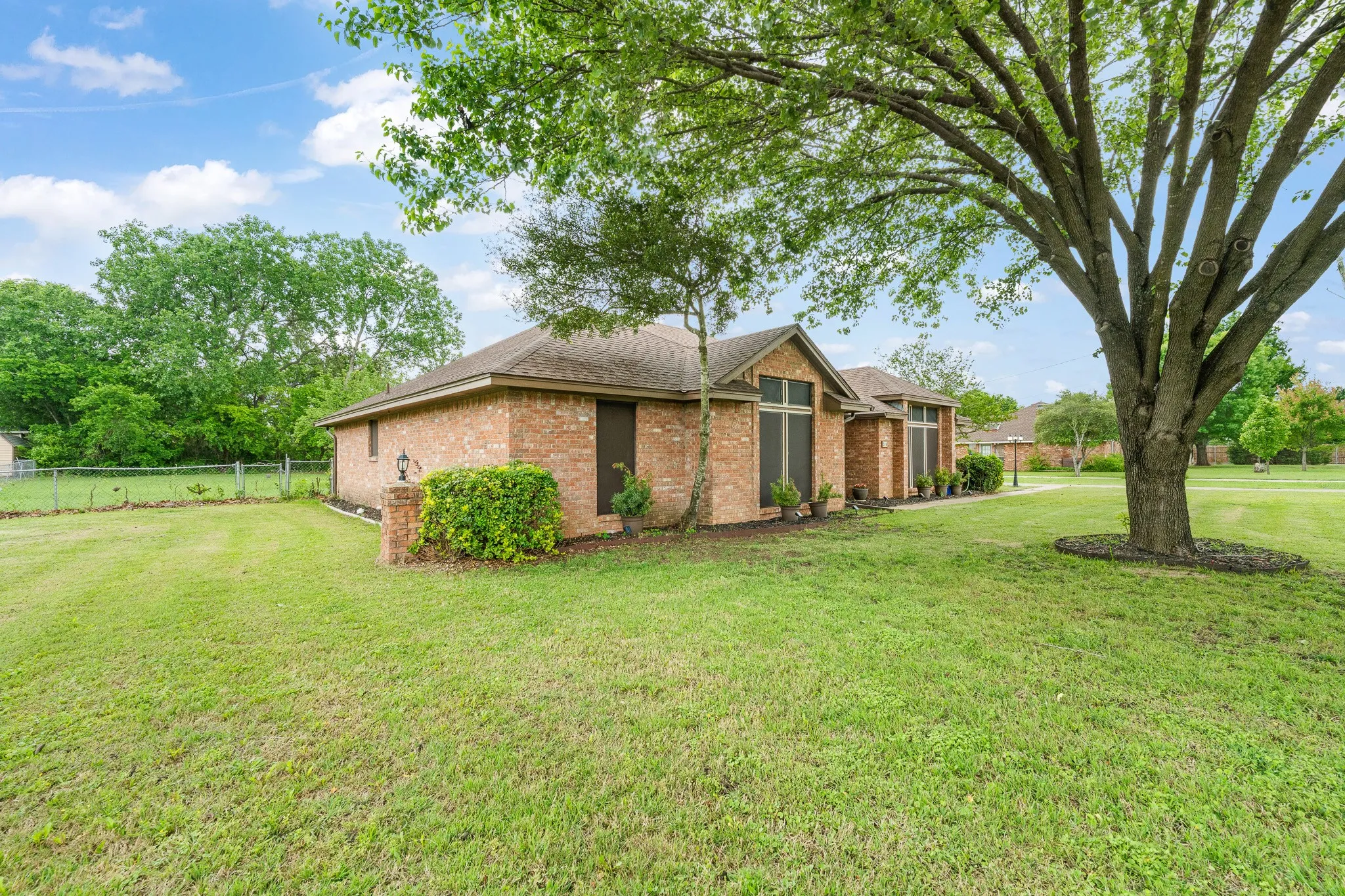 The property features a brick exterior, a well-maintained lawn, and mature trees providing shade