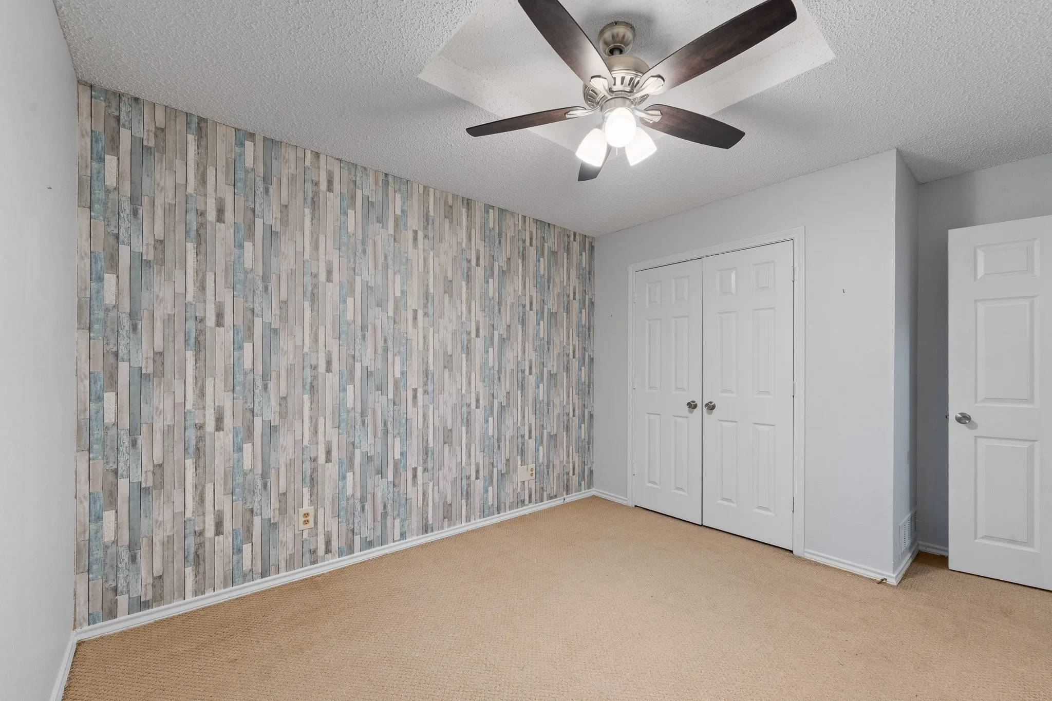 This room features an accent wall with a wood plank design, a ceiling fan with integrated lighting, and carpeted flooring