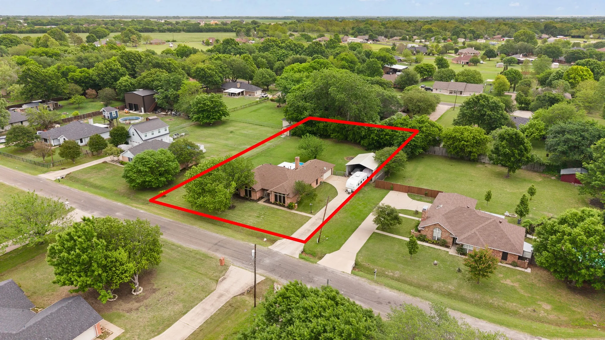 The property features a ranch-style home with an attached garage, a long paved driveway, and a detached carport