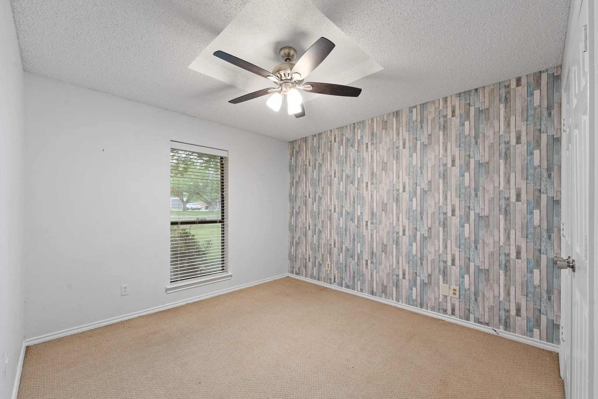 This room features a window with blinds, carpeted flooring, and a ceiling fan for comfort