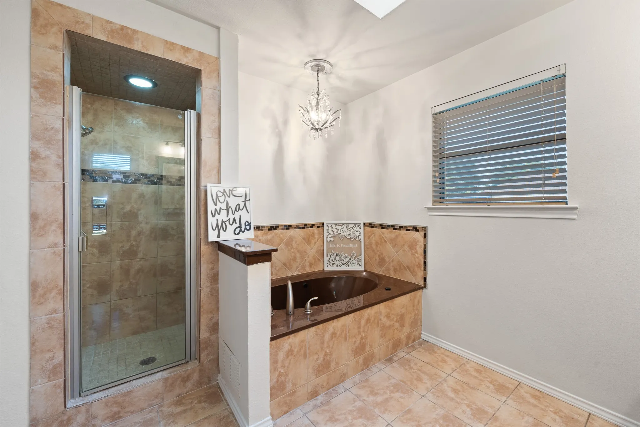 Tiled walk-in shower with a glass enclosure, a built-in soaking tub with tiled surround, and a decorative chandelier