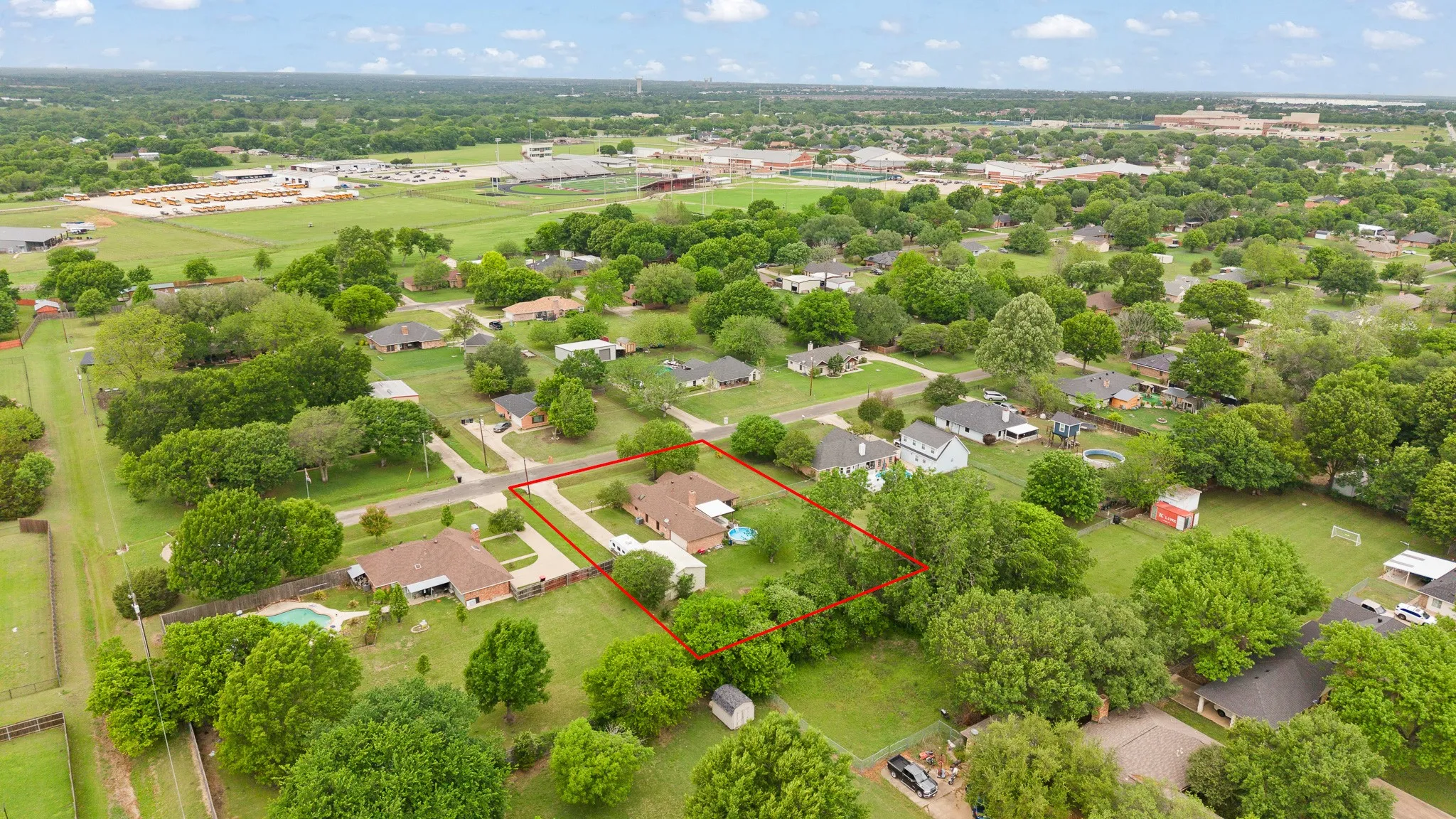 Aerial view showcasing the property, marked by a red outline, nestled within a verdant neighborhood with extensive green spaces and mature trees