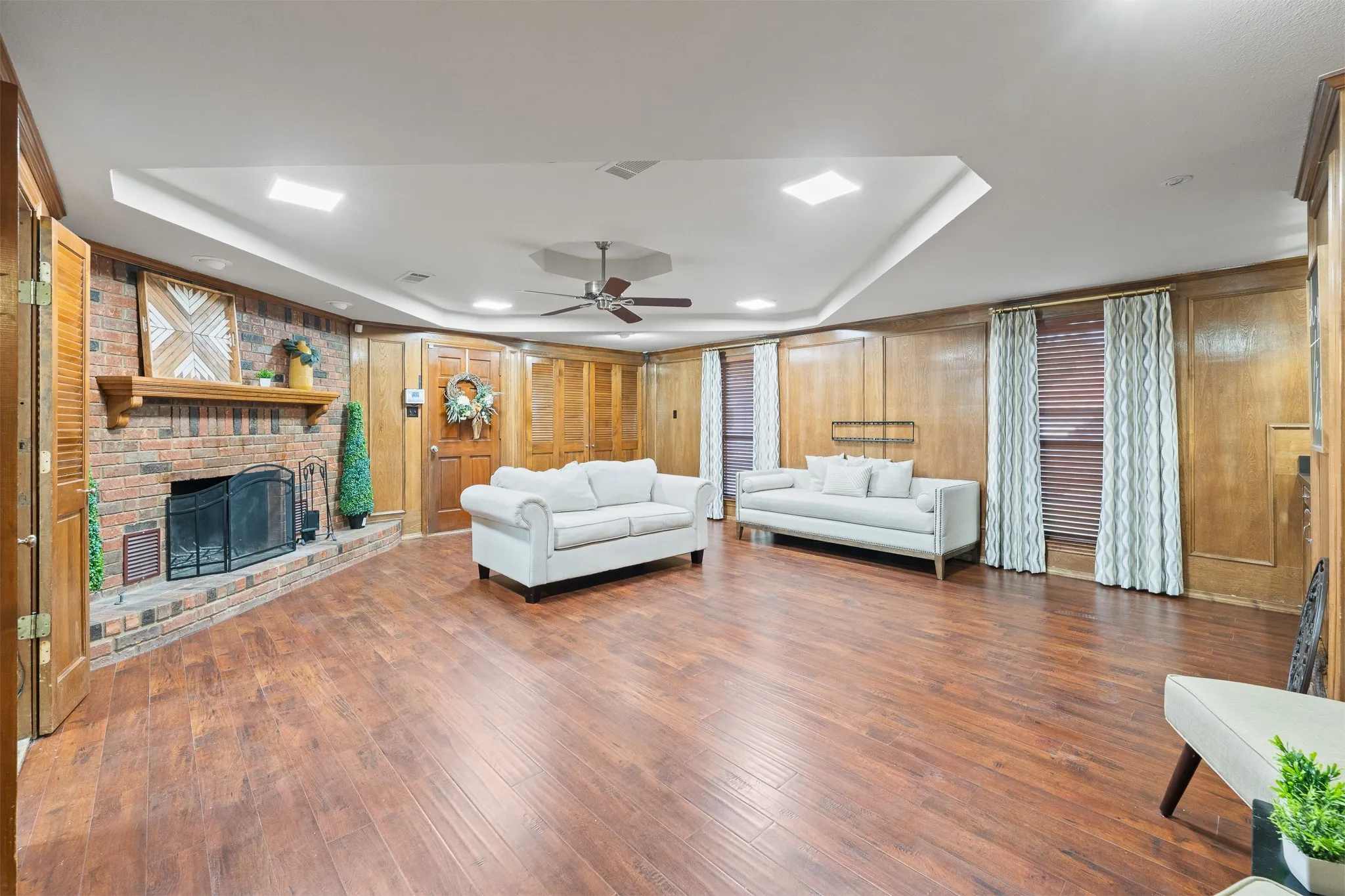 Spacious room featuring wood-finish flooring, a brick fireplace with a hearth, wood paneling, and an inset ceiling with recessed lighting