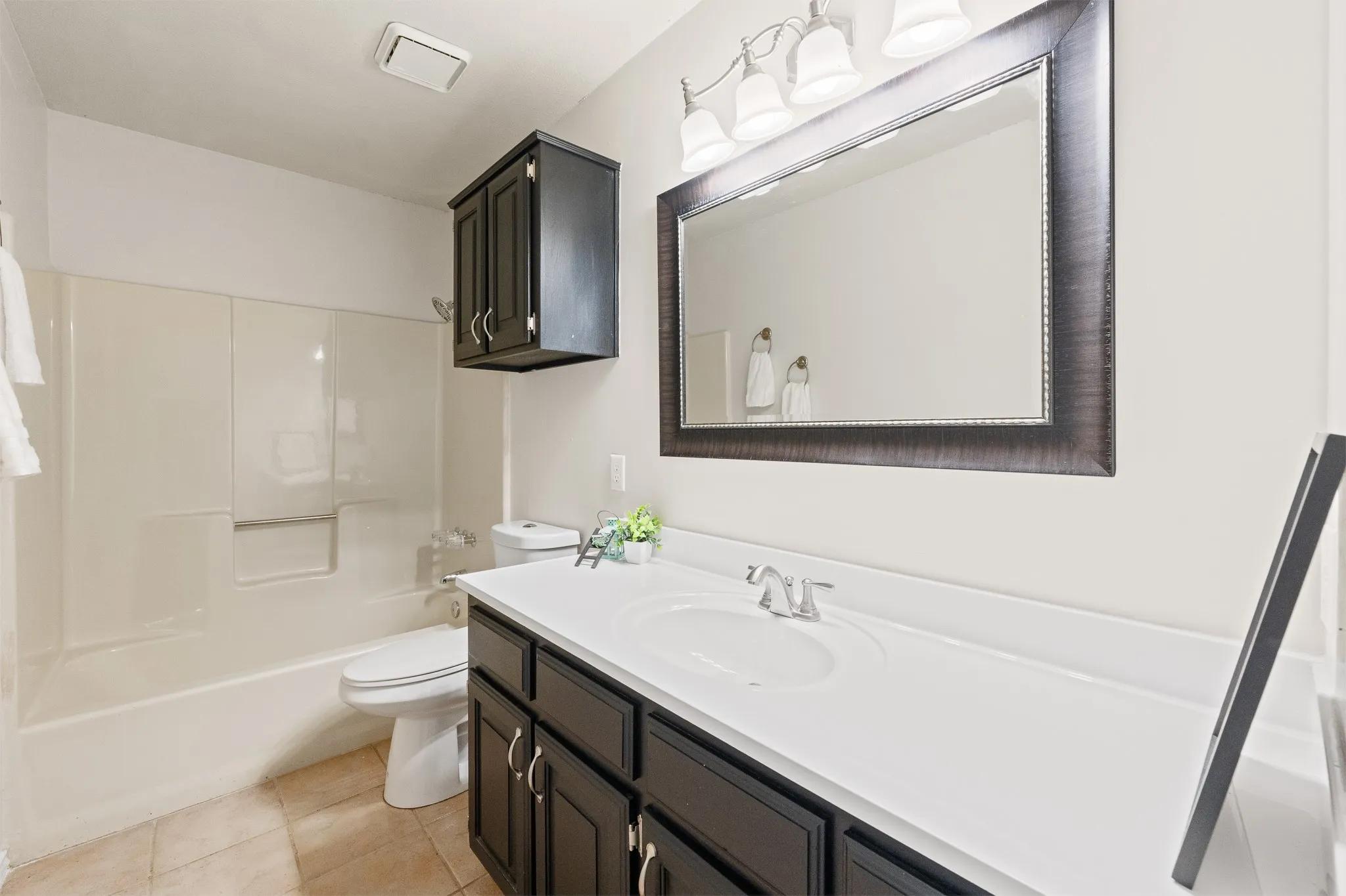 Vanity with integrated sink, dark wood-finish cabinetry, and framed mirror with overhead lighting