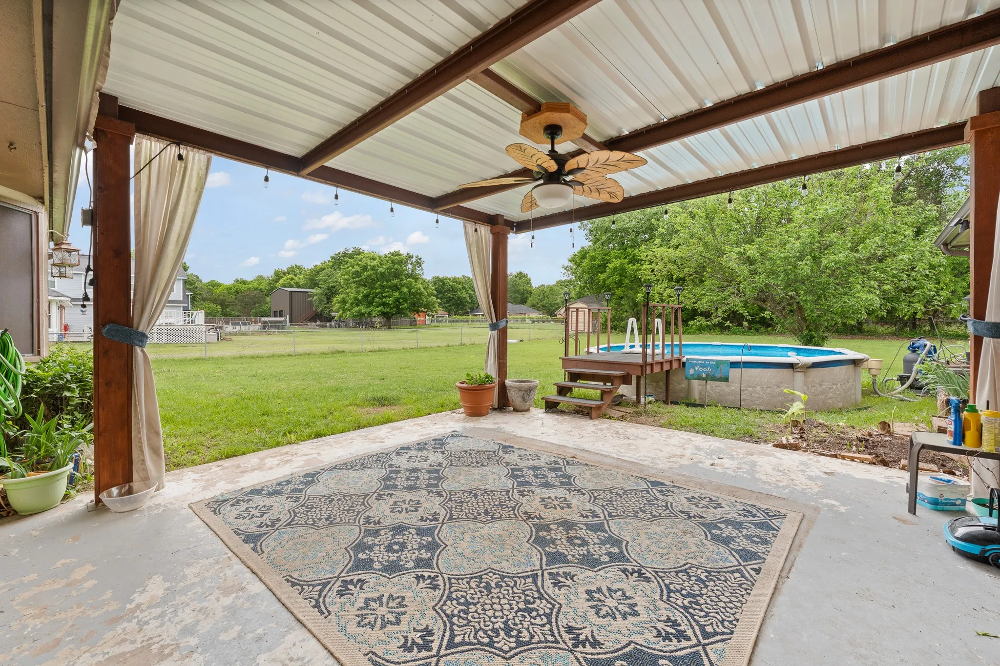 Covered patio area featuring a ceiling fan, string lights, and a view of the backyard with an above-ground pool