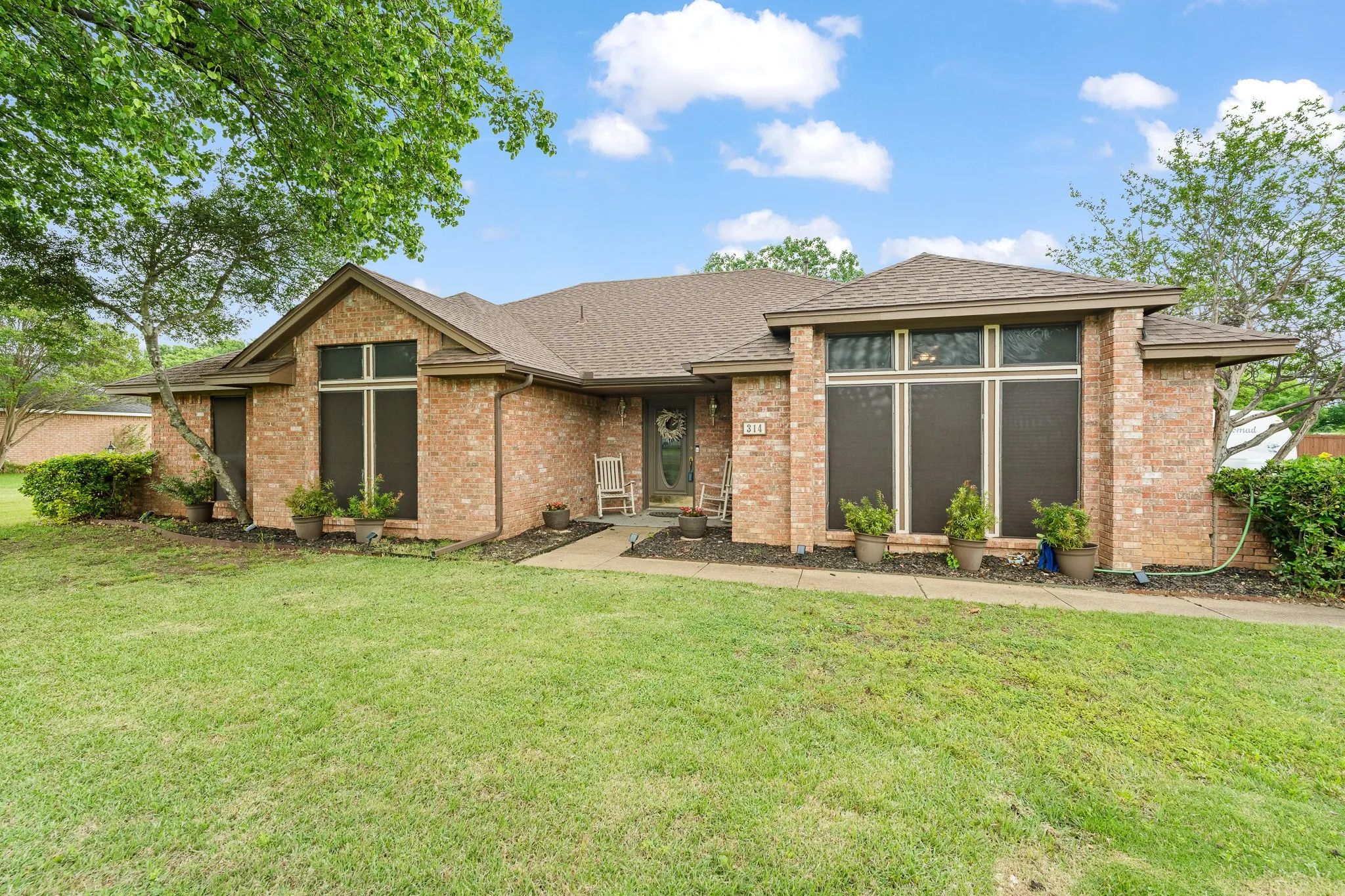 The property features a brick exterior, a well-maintained lawn, and mature trees
