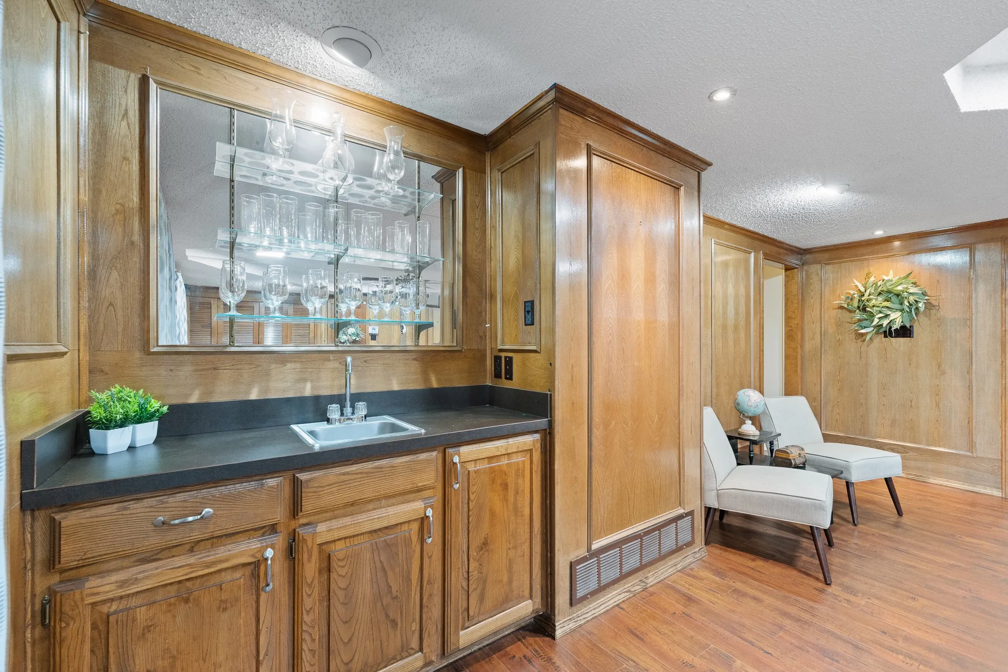 This space features extensive wood paneling, a wet bar with a built-in sink and shelving, and recessed lighting