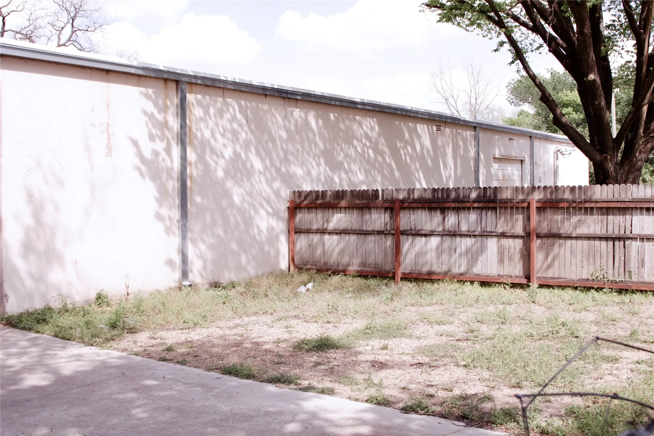 The property features an exterior wall with a metal roofline, a wooden fence, and a paved surface