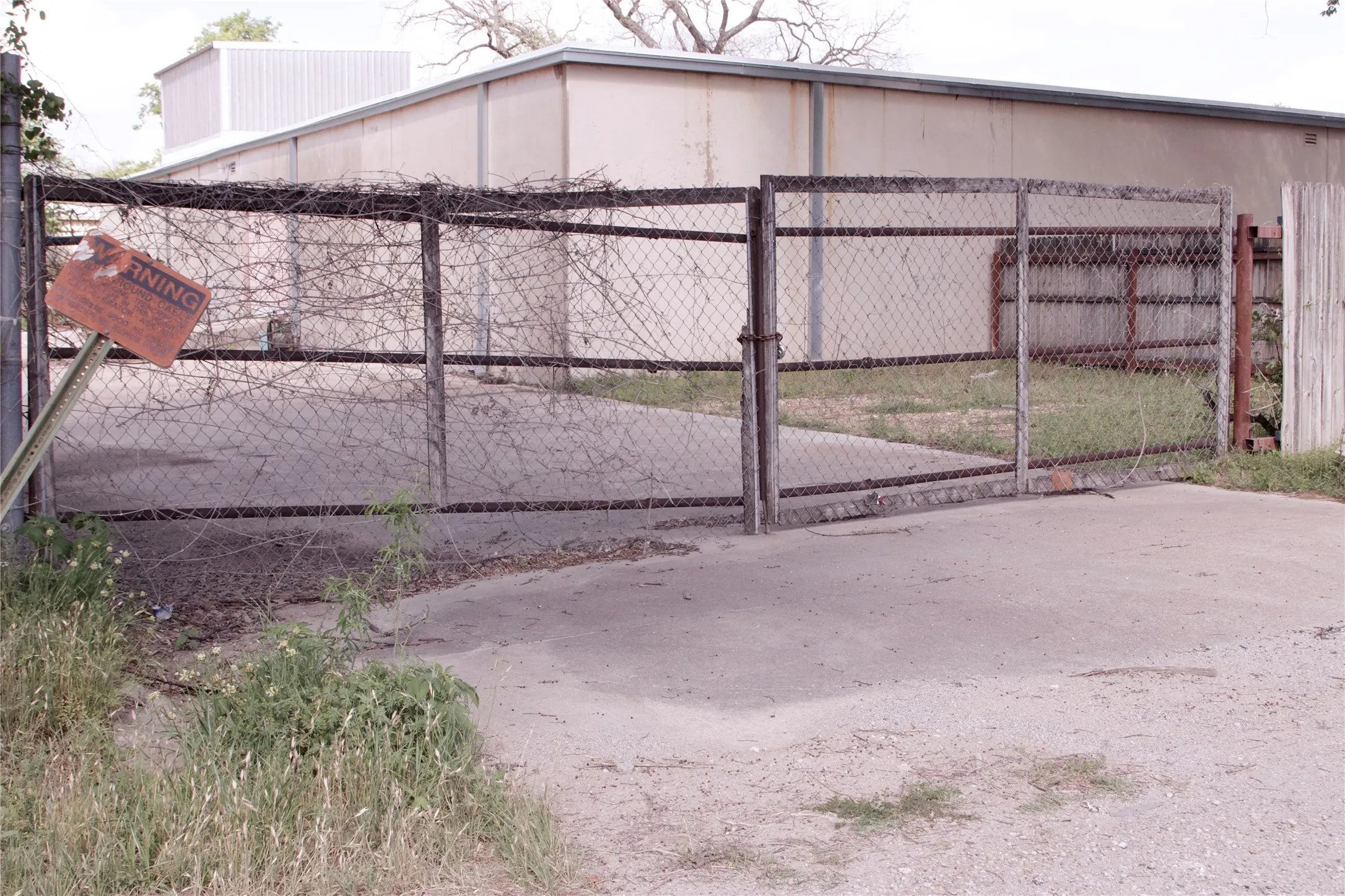 The property features a chain-link fence with a gate, a concrete pad, and a building with a light-colored exterior and a corrugated metal roof
