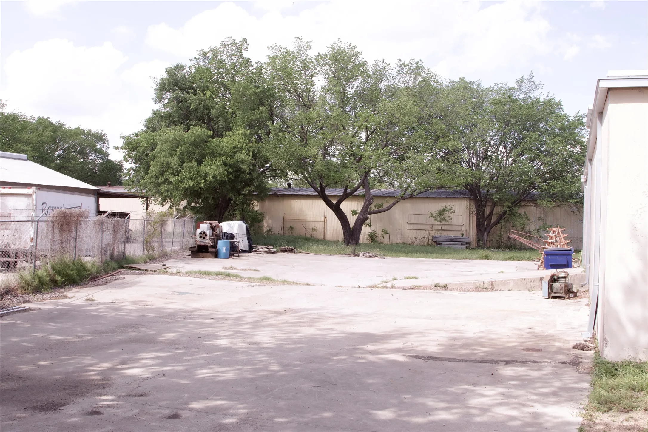 The property features a concrete paved area with mature trees and a fenced perimeter