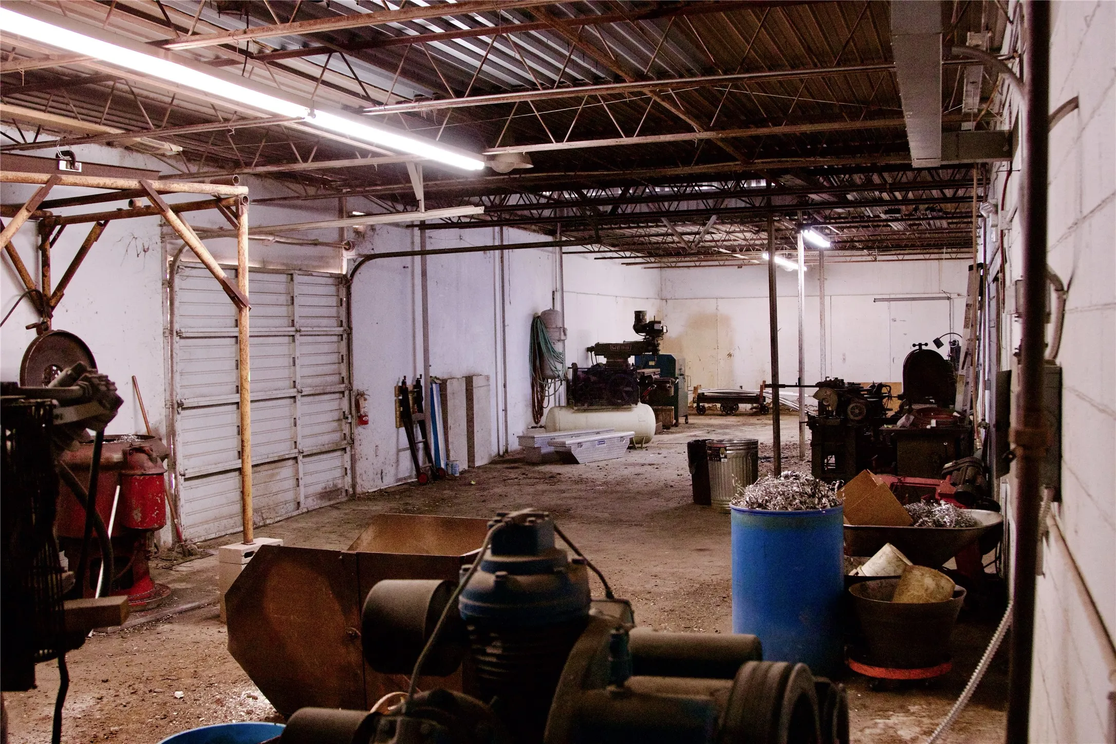 Industrial space featuring exposed ceiling joists, fluorescent lighting, and a large roll-up door