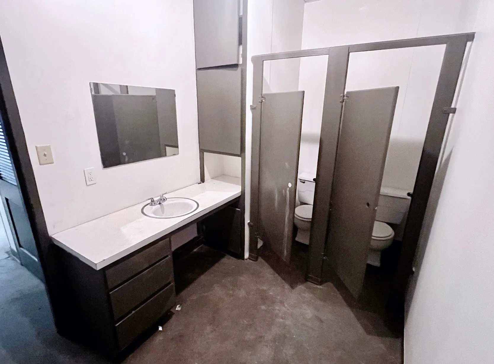 The bathroom features a vanity with a white countertop and an integrated sink, a wall-mounted mirror, and separate toilet stalls