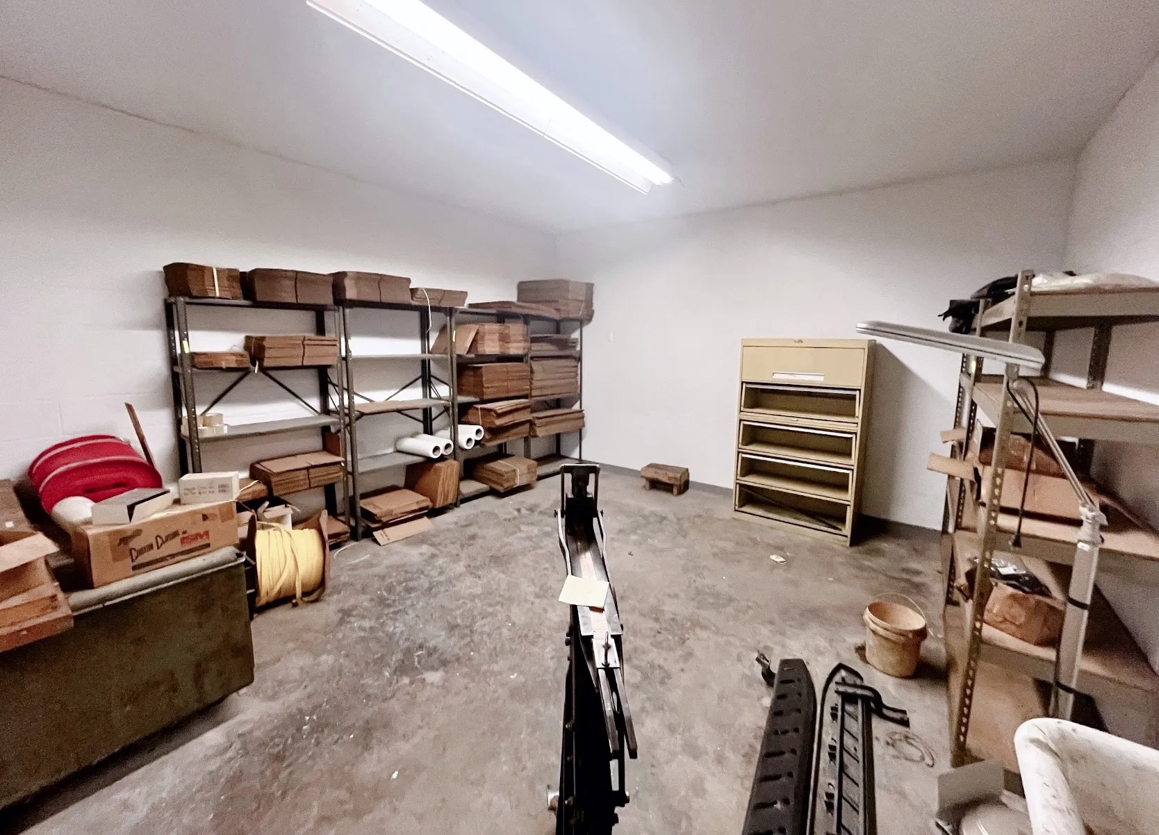 The property features a spacious room with concrete flooring, illuminated by overhead fluorescent lighting