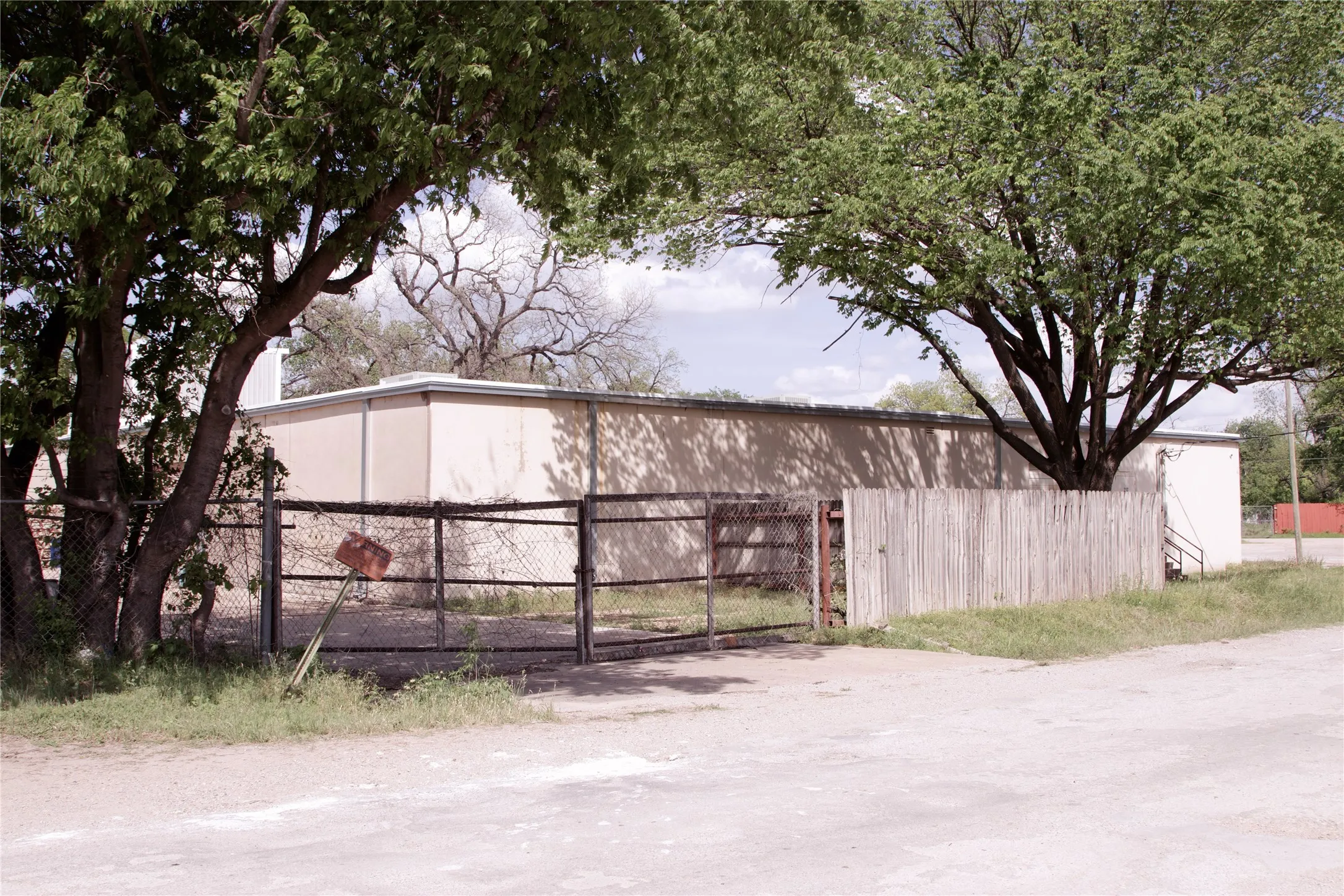 The property features a fence with a gate, complemented by mature trees and a building with tan siding