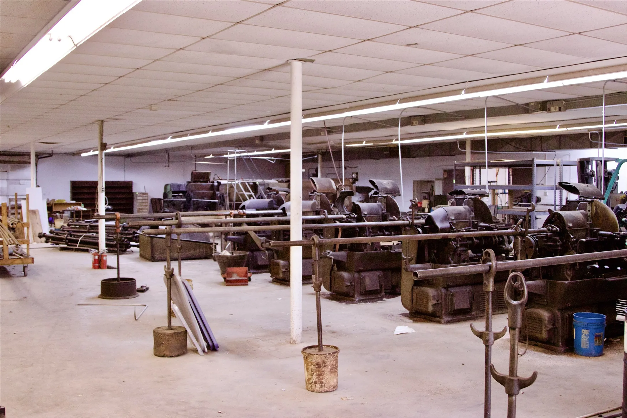Spacious interior with an exposed concrete floor, drop ceiling with fluorescent lighting, and visible support columns