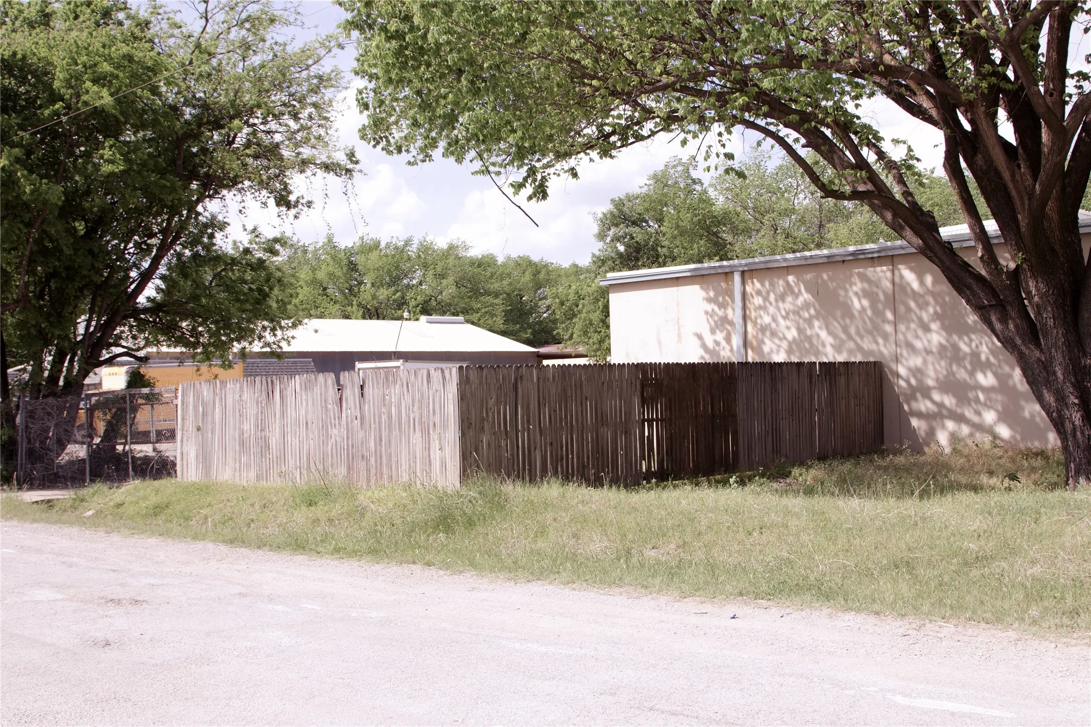 The property features a wooden privacy fence, a gravel road frontage, and a grassy area
