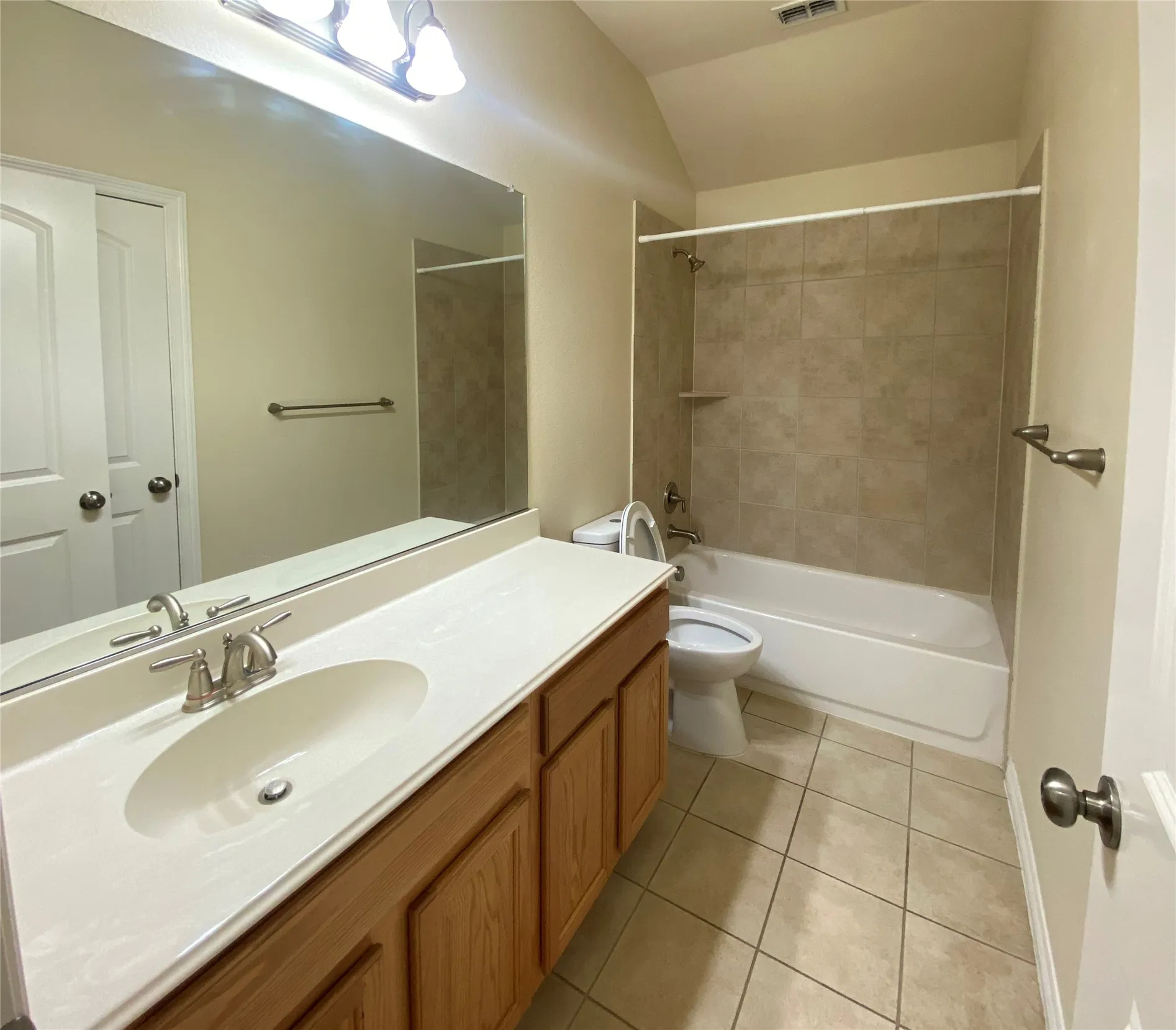 2nd Bathroom featuring a wood-finish vanity with an integrated sink and light-colored countertop, a large wall-mounted mirror, brushed nickel fixtures, a tub-shower combination with tile surround, and neutral tile flooring
