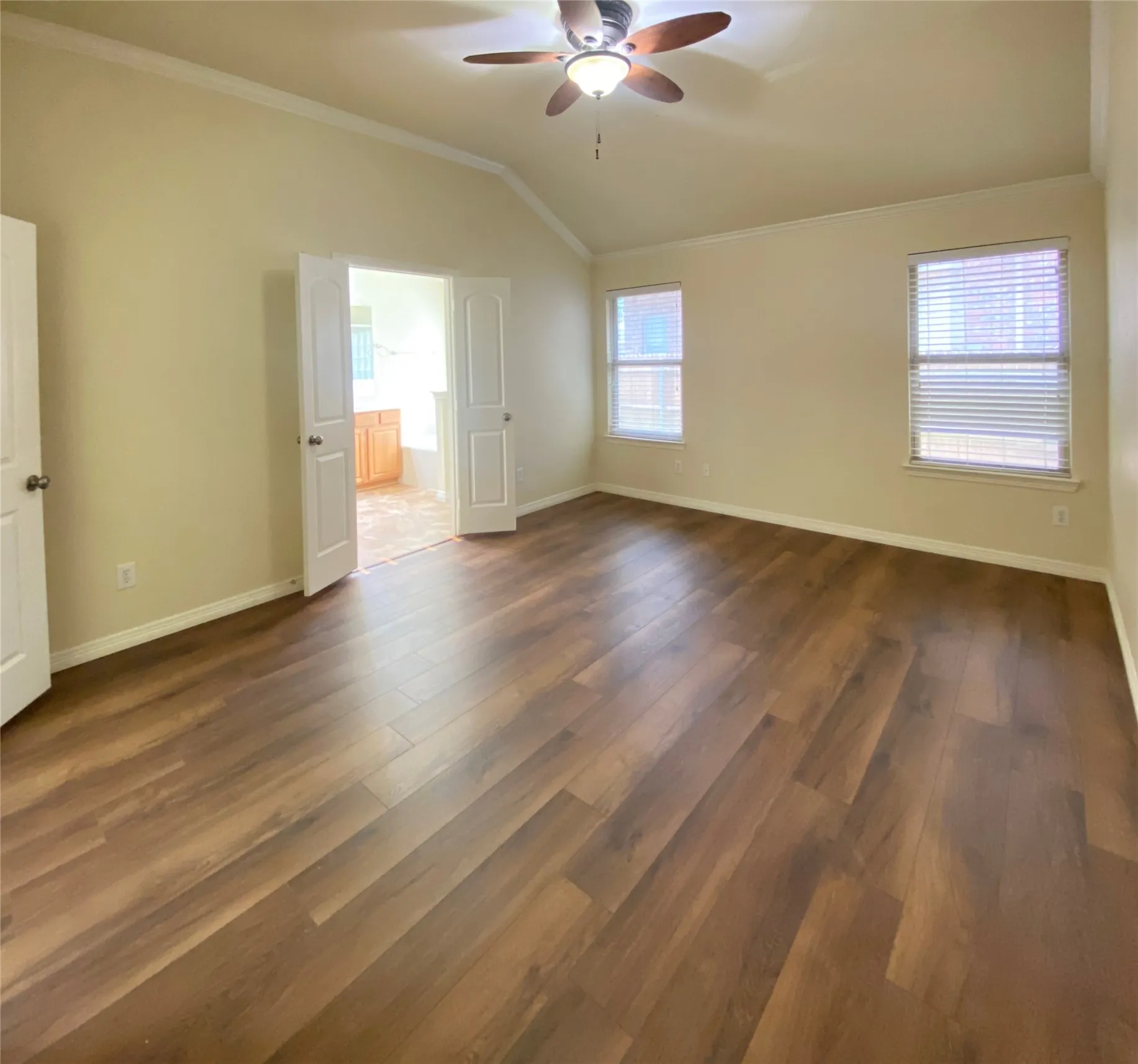 Spacious master bedroom featuring wood-finish flooring, vaulted ceilings, and crown molding
