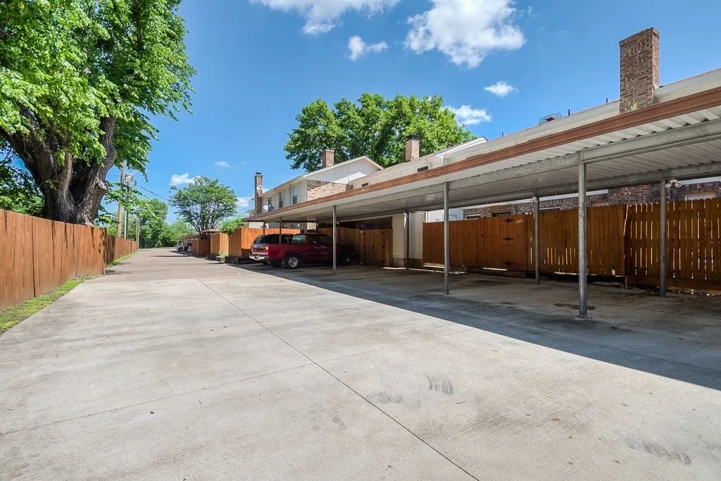 The property features a concrete paved parking area with covered parking spaces, bordered by a wooden fence
