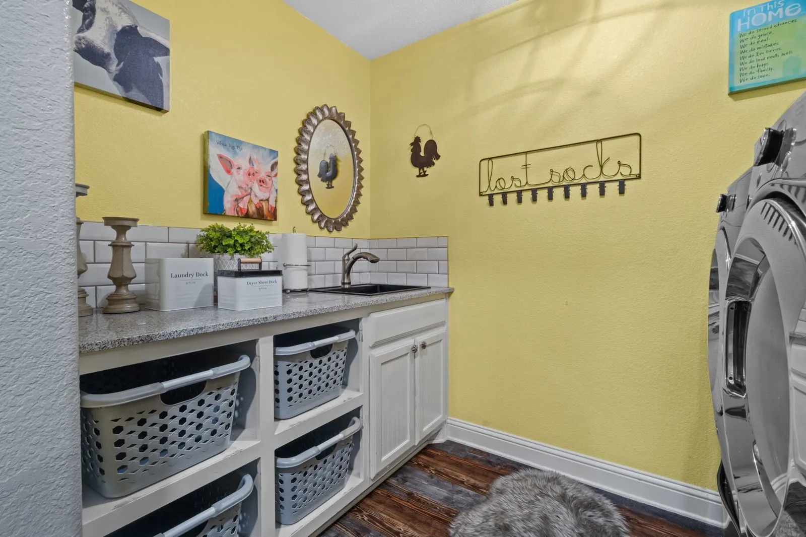 This cheerful, well-organized laundry room is tucked behind a charming farm door and features great storage, a convenient sink, a stylish tile backsplash, and warm farmhouse-inspired luxury vinyl floors.