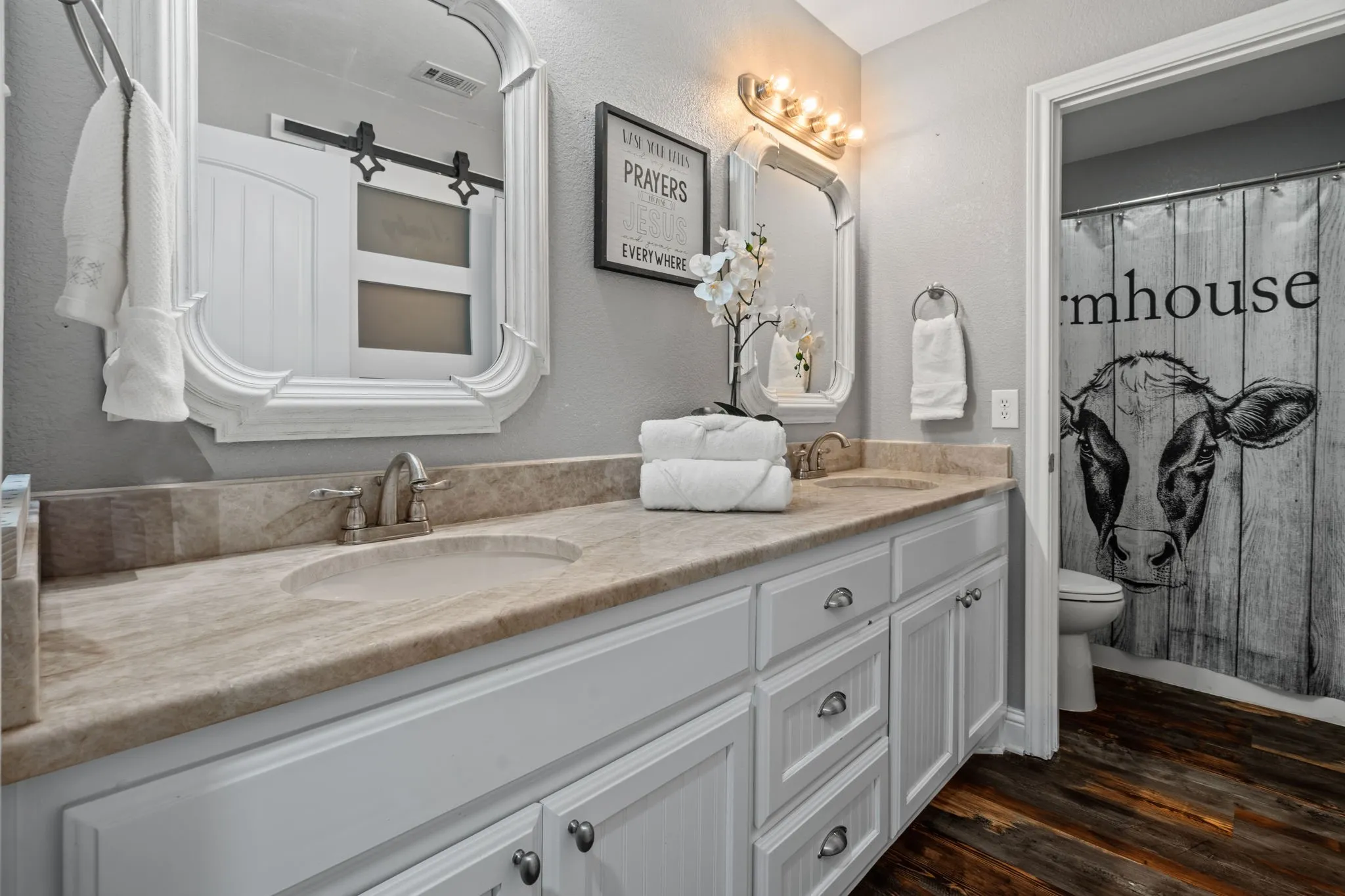 Bright, beautifully updated ensuite featuring dual sinks, framed mirrors, fresh finishes, warm farmhouse-inspired luxury vinyl floors, and shower with tub.