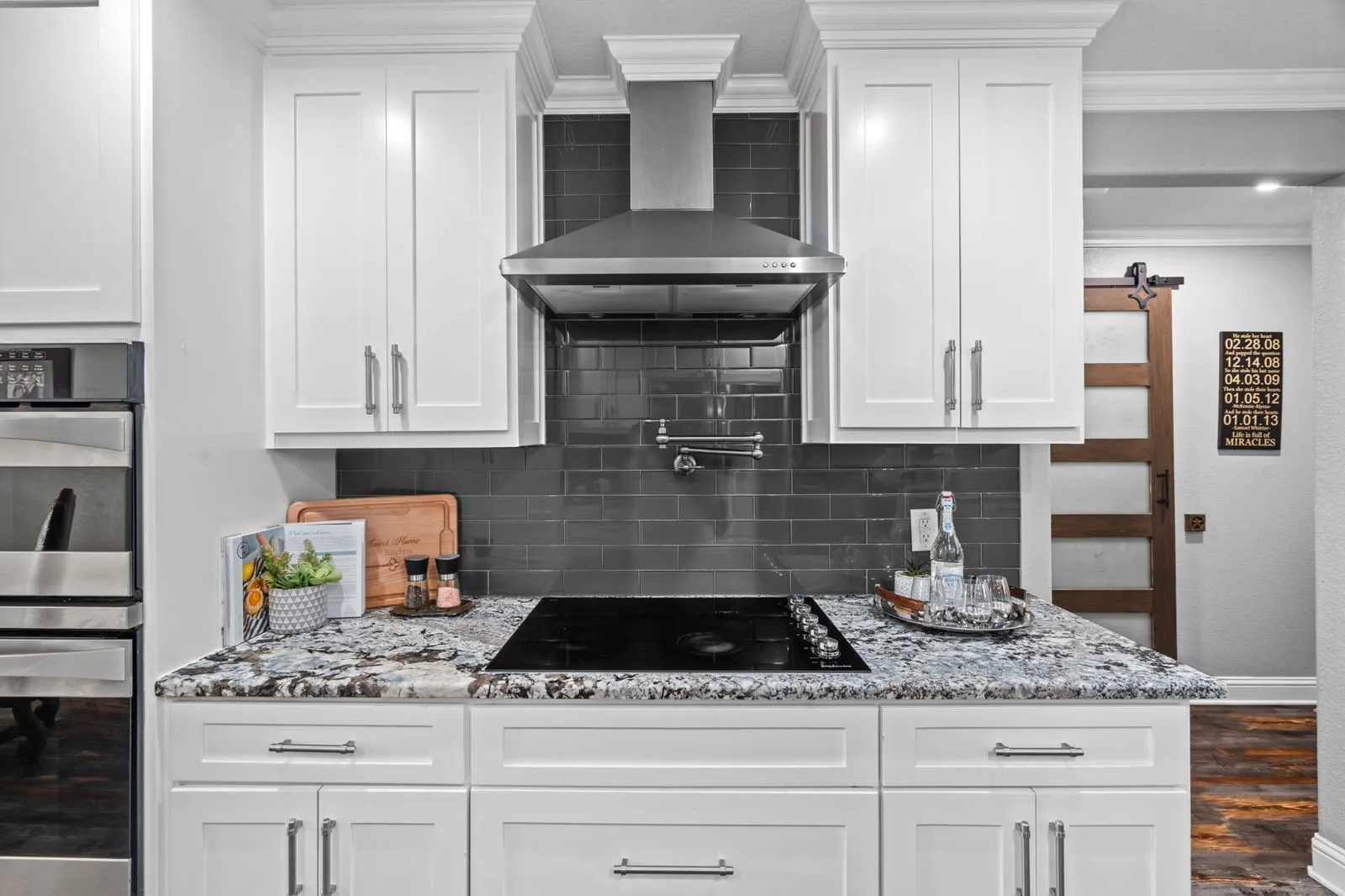 Soft, beautifully coordinated tones blend the white cabinetry, granite counters, and sleek backsplash for a warm, inviting kitchen aesthetic.