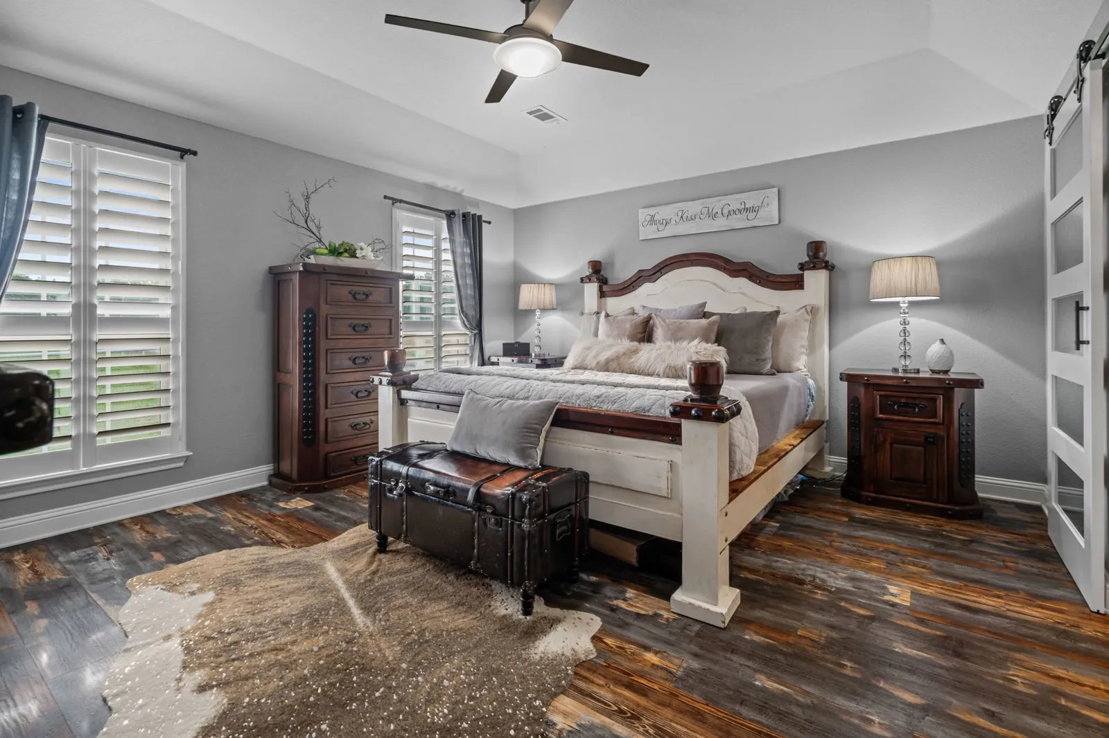 This lovely, serene primary bedroom features vaulted ceilings, a ceiling fan, warm tones, and windows framing scenic views for a peaceful retreat-like atmosphere.