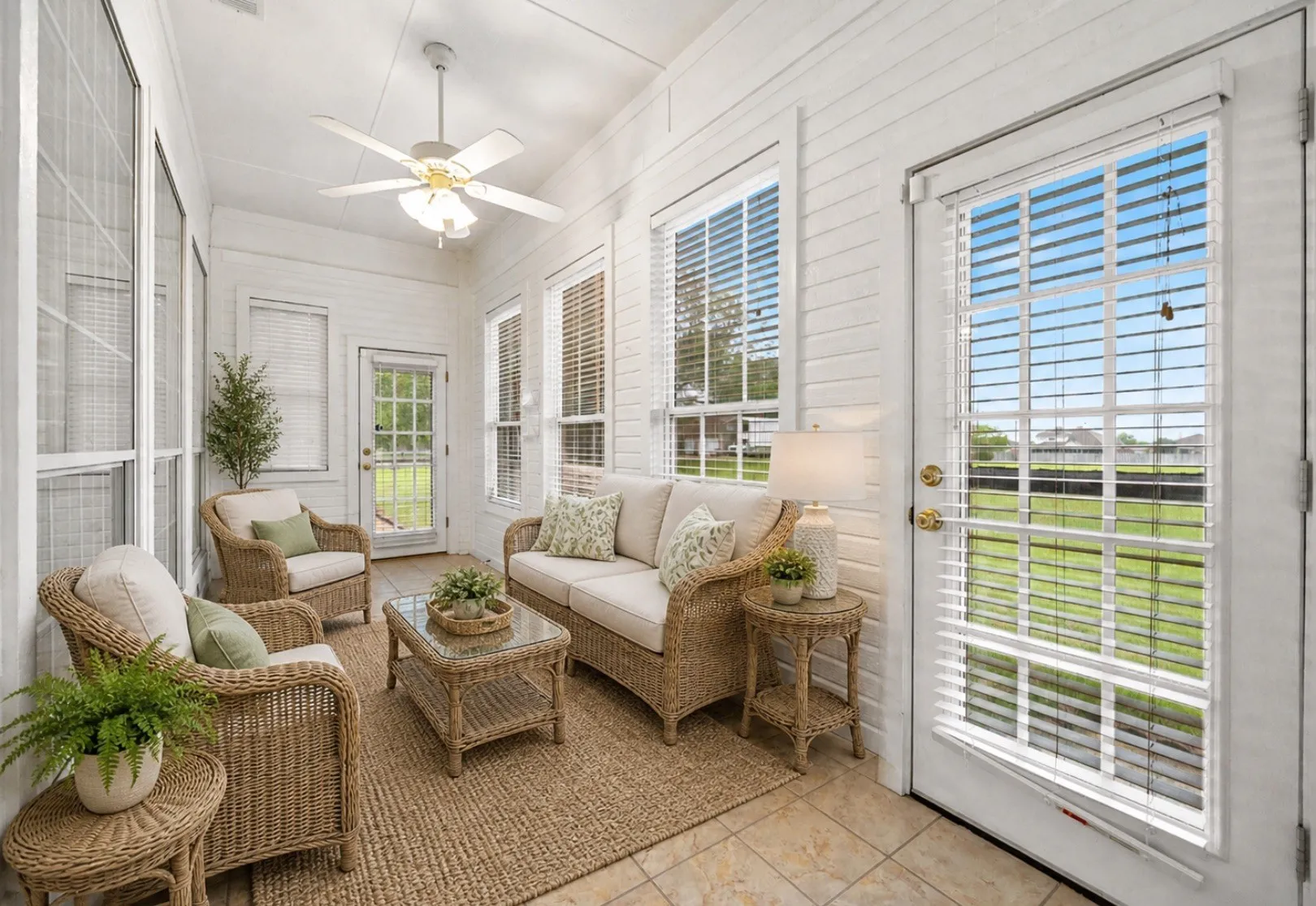 Sunroom featuring tile flooring, white horizontal paneling, multiple windows with blinds, a ceiling fan, and access to the exterior