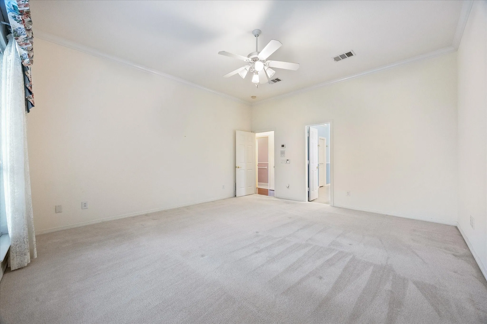 This spacious room features neutral-toned carpet, a ceiling fan, and crown molding