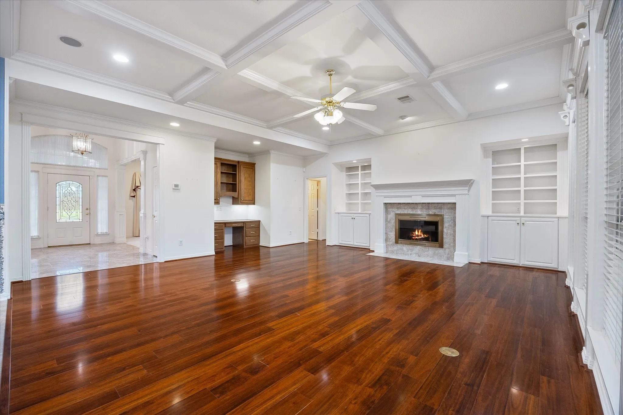 Spacious living area featuring rich hardwood flooring, a coffered ceiling, and a fireplace with a stone surround flanked by built-in shelving and cabinetry