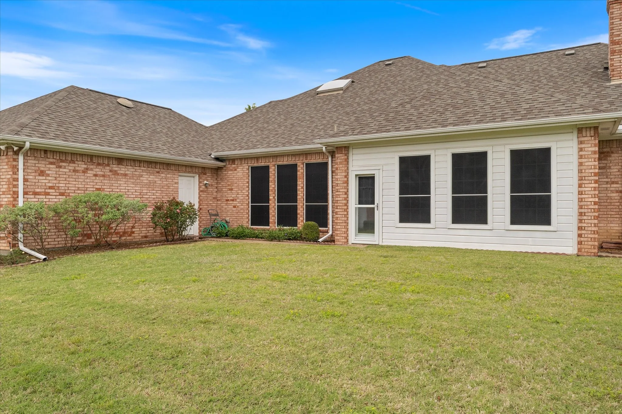 The property features a brick exterior, a well-maintained lawn, and a sunroom with white siding and multiple windows