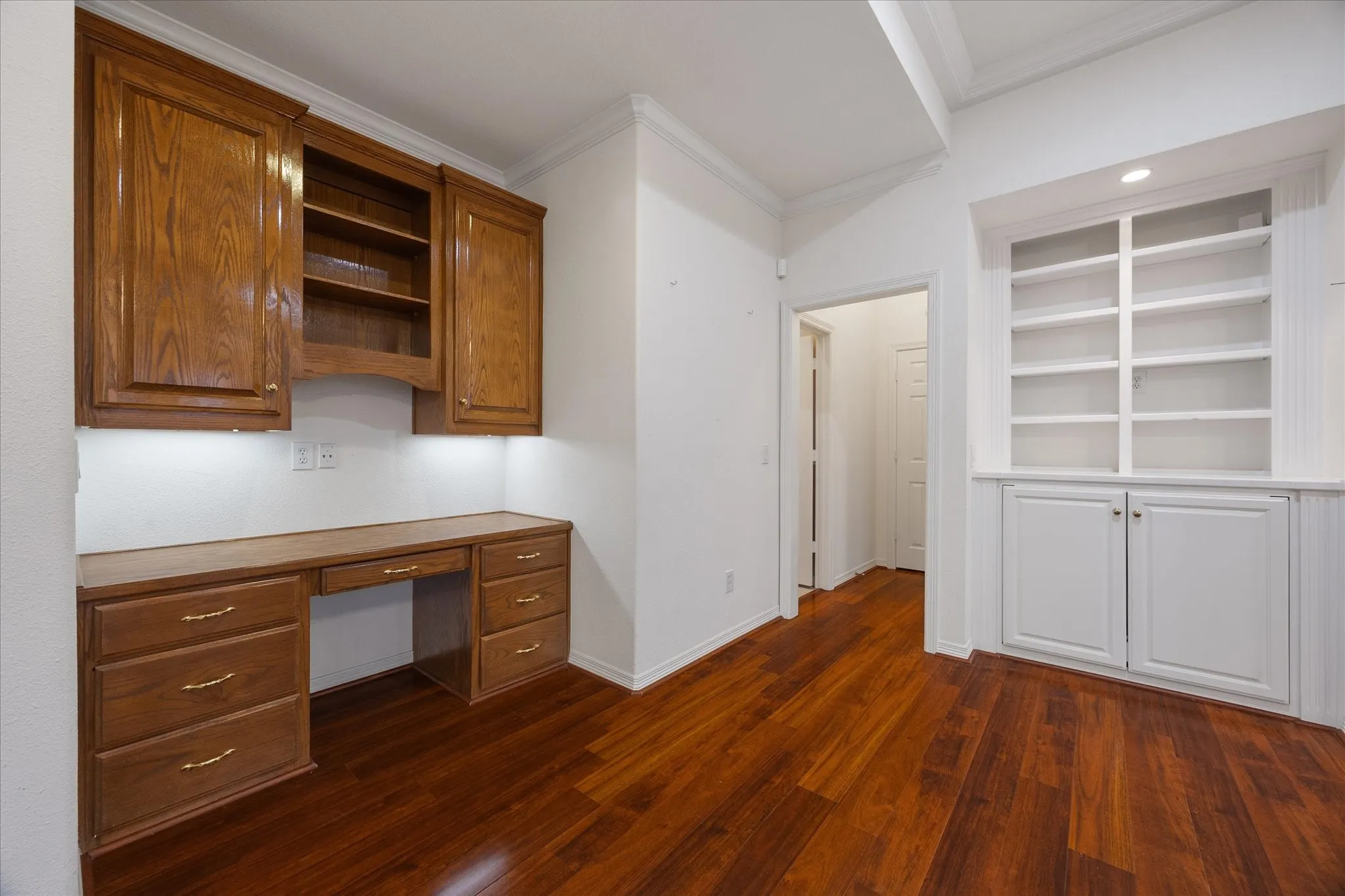 This room features rich hardwood floors, an integrated wooden desk with storage, and built-in white shelving for display and storage