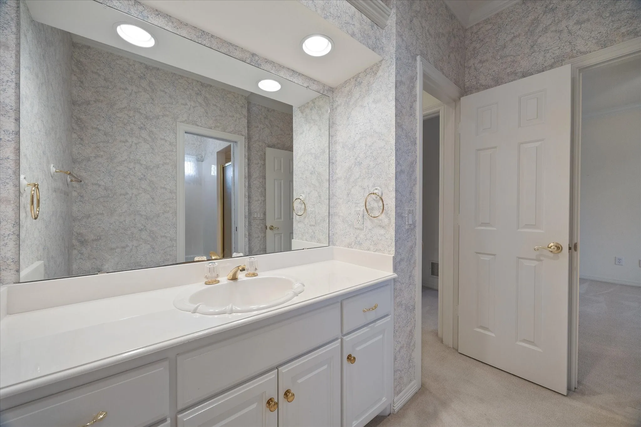 The bathroom features a spacious vanity with a white countertop and white cabinetry with gold-toned​​‌​​​​‌​​‌‌​‌‌​​​‌‌​‌​‌​‌​​​‌​​ hardware