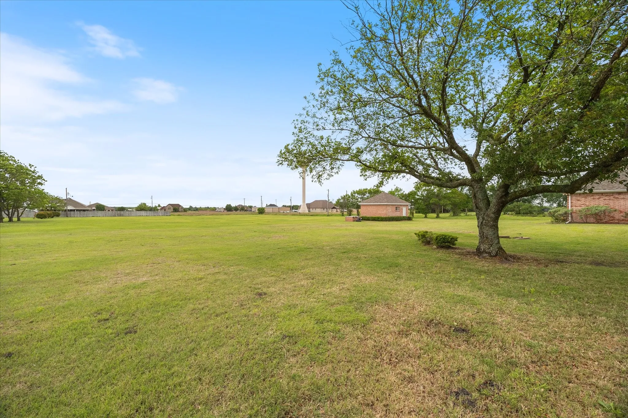 Expansive green lawn with a mature tree, offering open space and views of nearby properties with brick exteriors under a clear sky