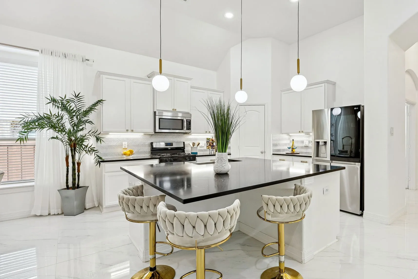The kitchen brings the drama with black quartz, white cabinetry, gold accents, pendant lighting, and an oversized  island.