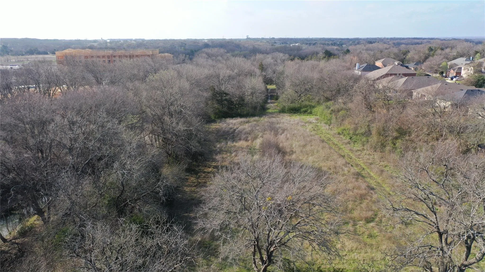 Expansive parcel with mature trees and a cleared central area, offering views of surrounding development and residential properties