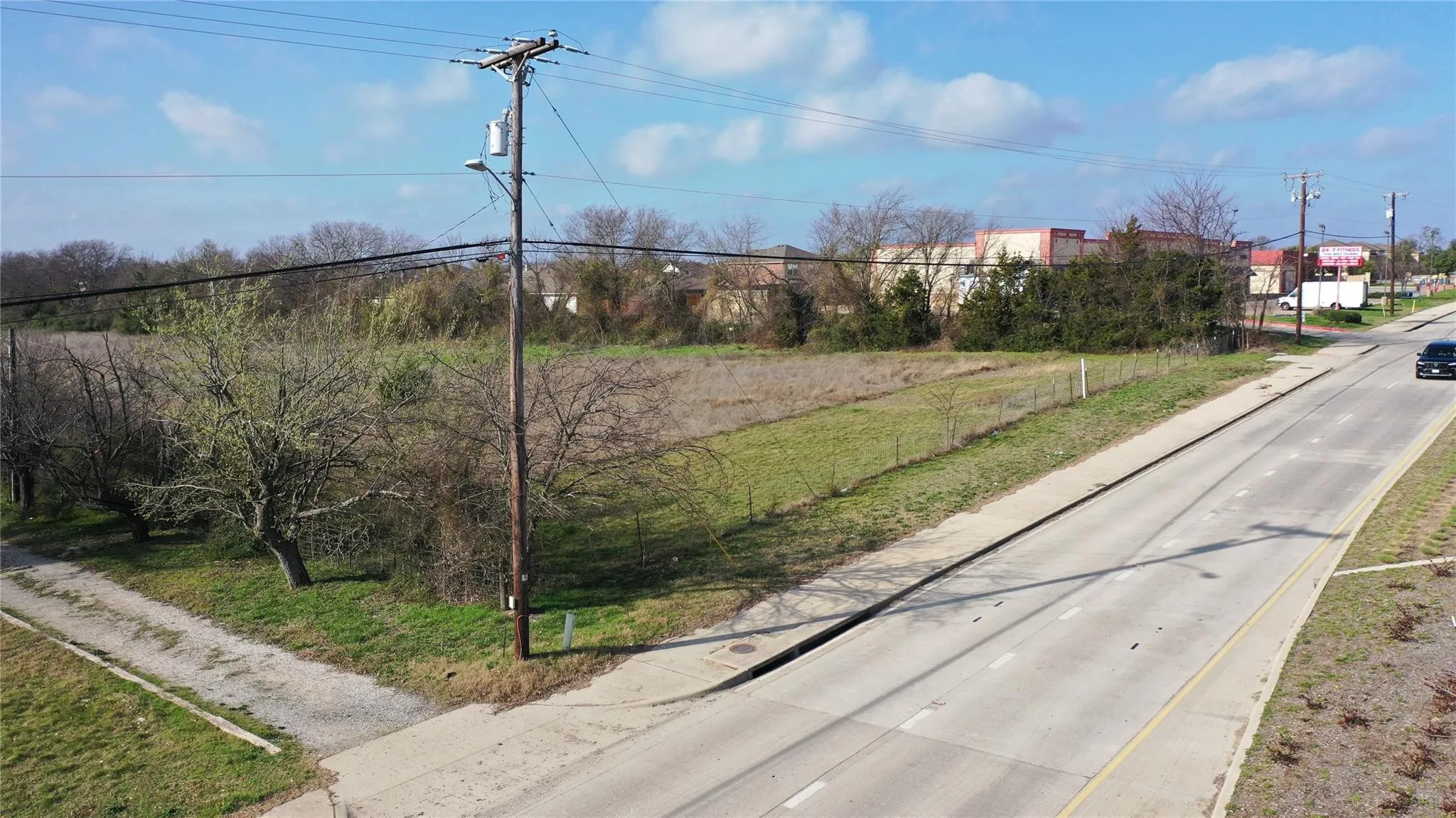 The property features a substantial undeveloped lot with a partial fence, mature trees, and direct frontage to a paved road
