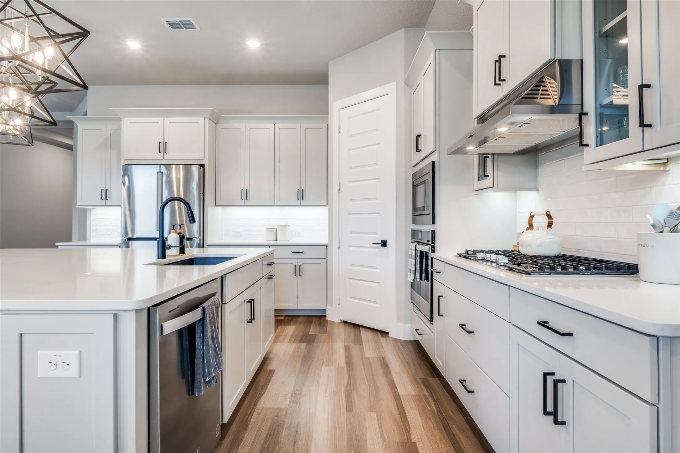 Modern kitchen featuring a large central island, farmhouse sink, stainless steel appliances, sleek white cabinetry with contemporary black hardware, and tiled backsplash. Perfectly arranged for cooking and entertaining.