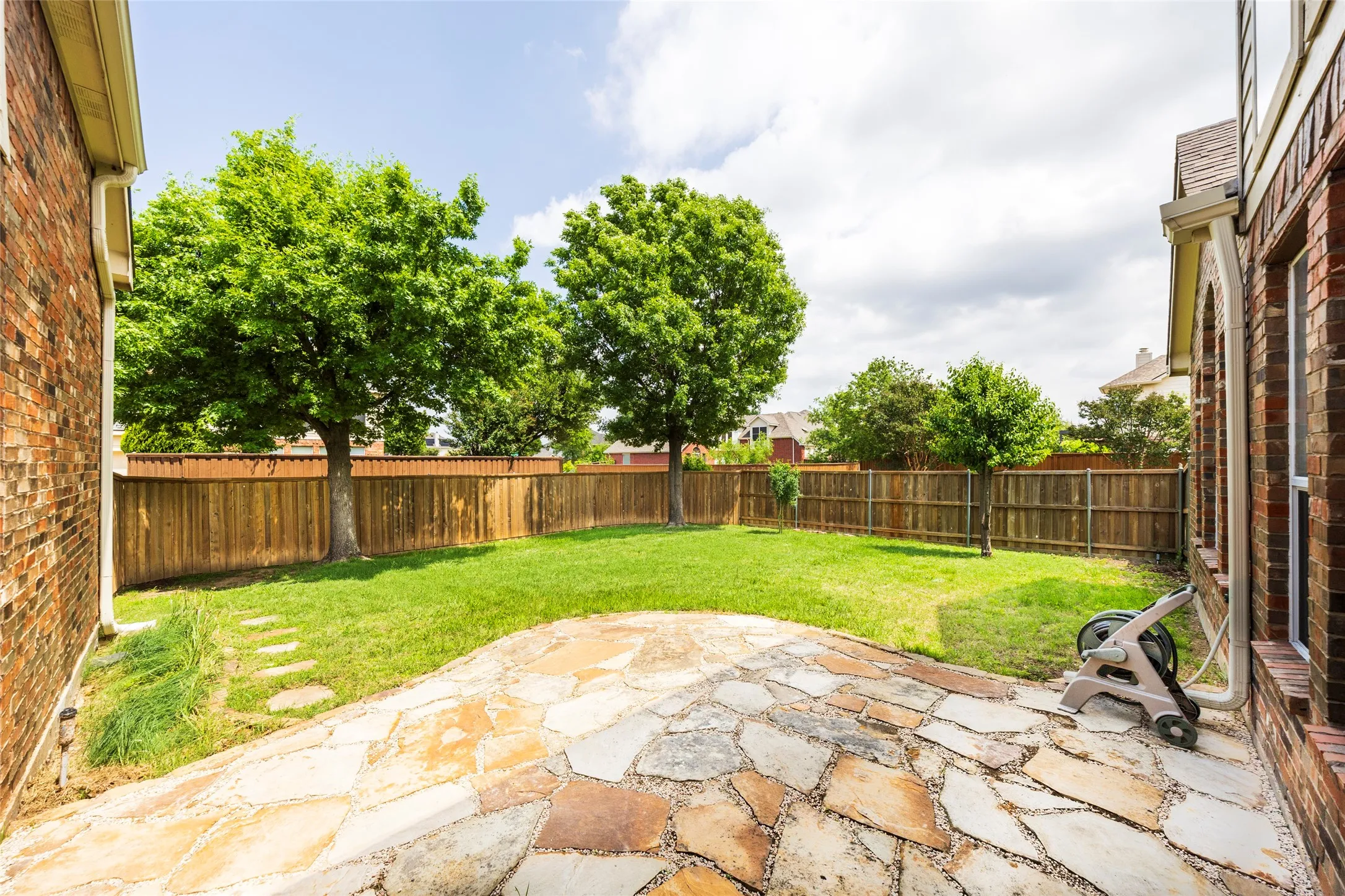 The property features a spacious backyard with a stone patio, a well-maintained lawn, and mature trees providing shade