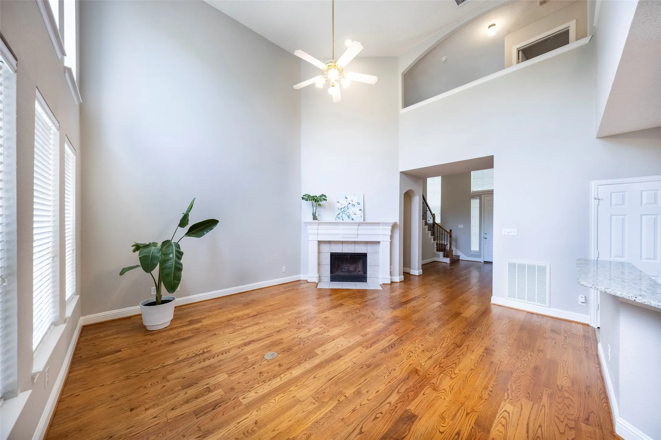 The living area features high ceilings, hardwood flooring, a fireplace with a mantel, and windows with blinds