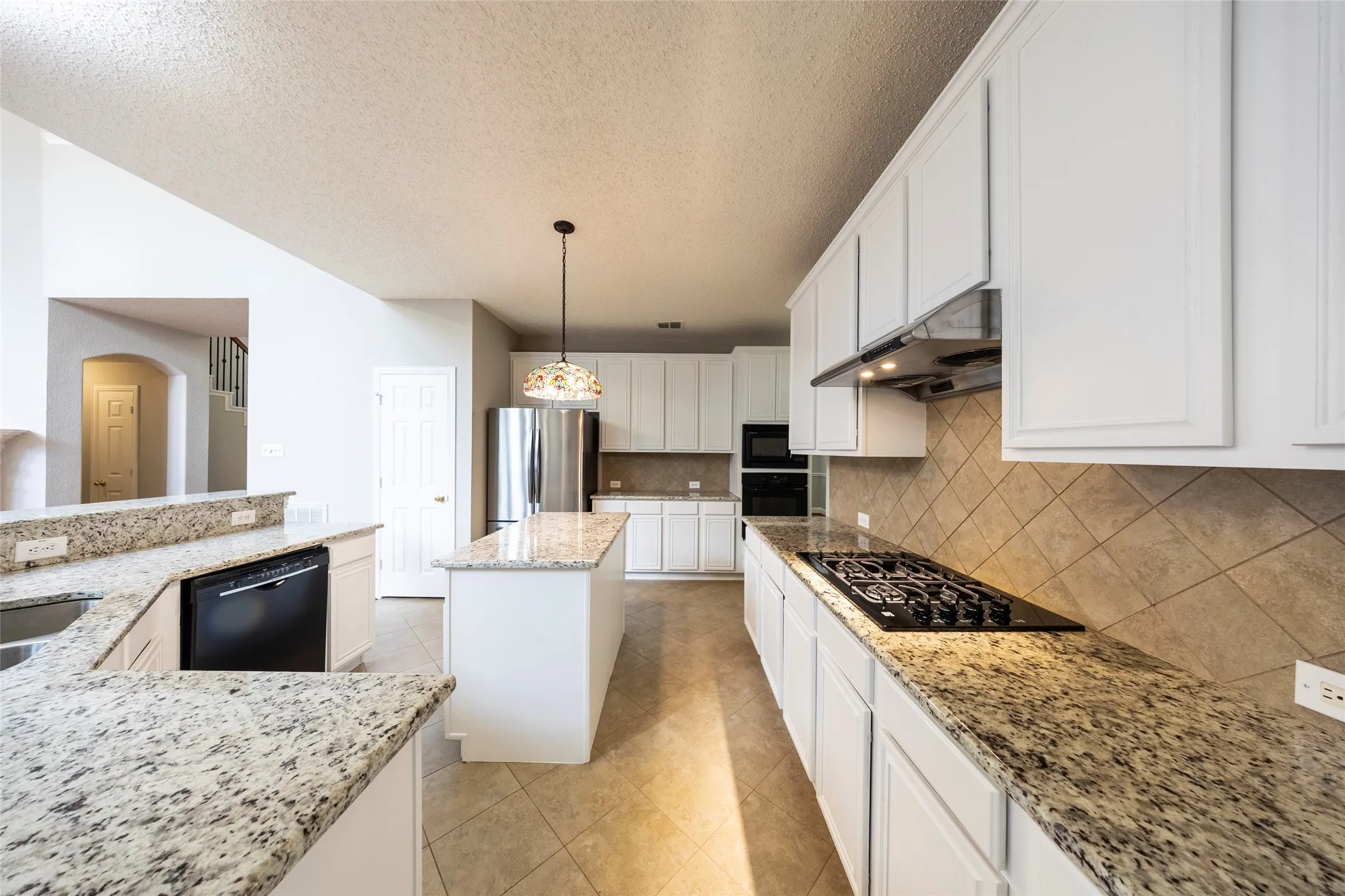 The kitchen features an island, white cabinetry, granite countertops, and tile flooring