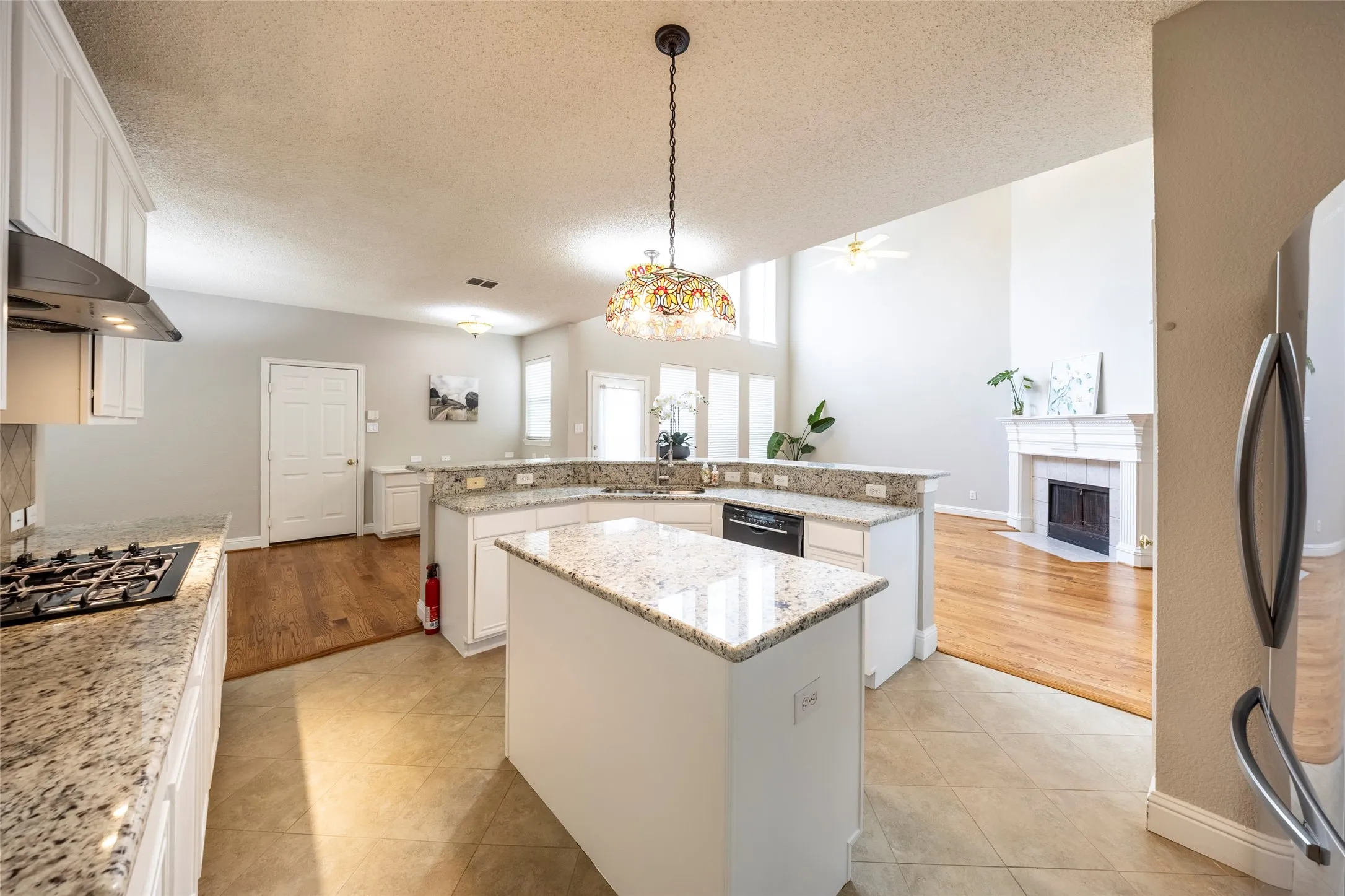 The kitchen features granite countertops, white cabinetry, a built-in gas cooktop with an overhead exhaust, and a center island
