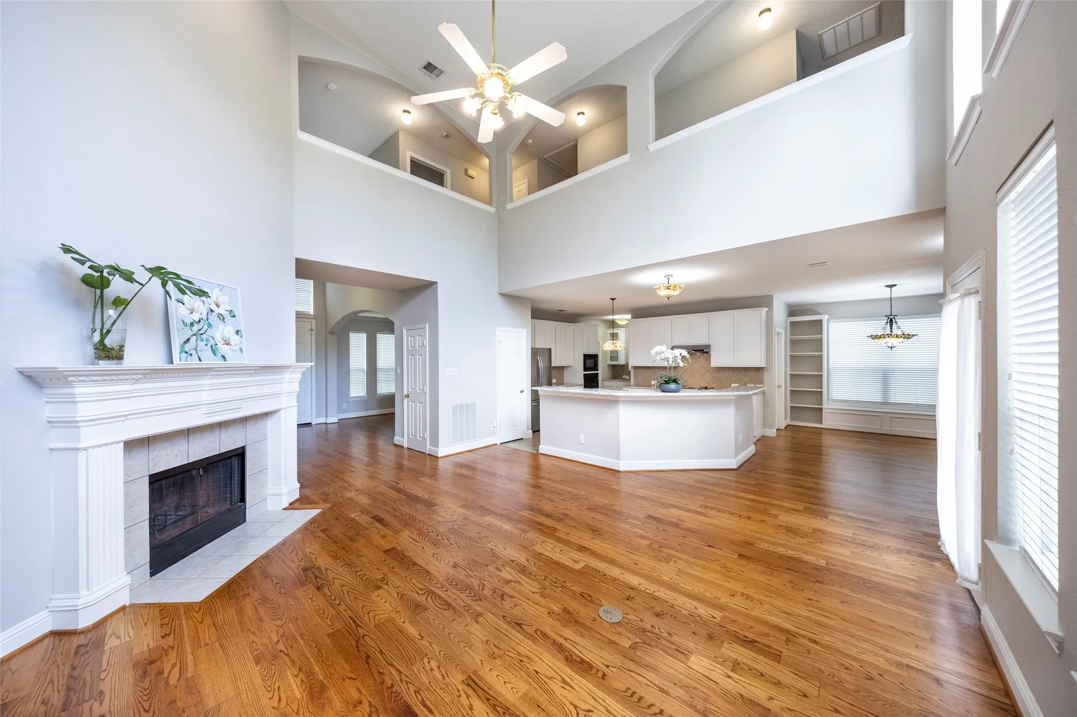 Spacious interior with vaulted ceilings, hardwood floors, a fireplace, and a kitchen featuring white cabinetry and an island