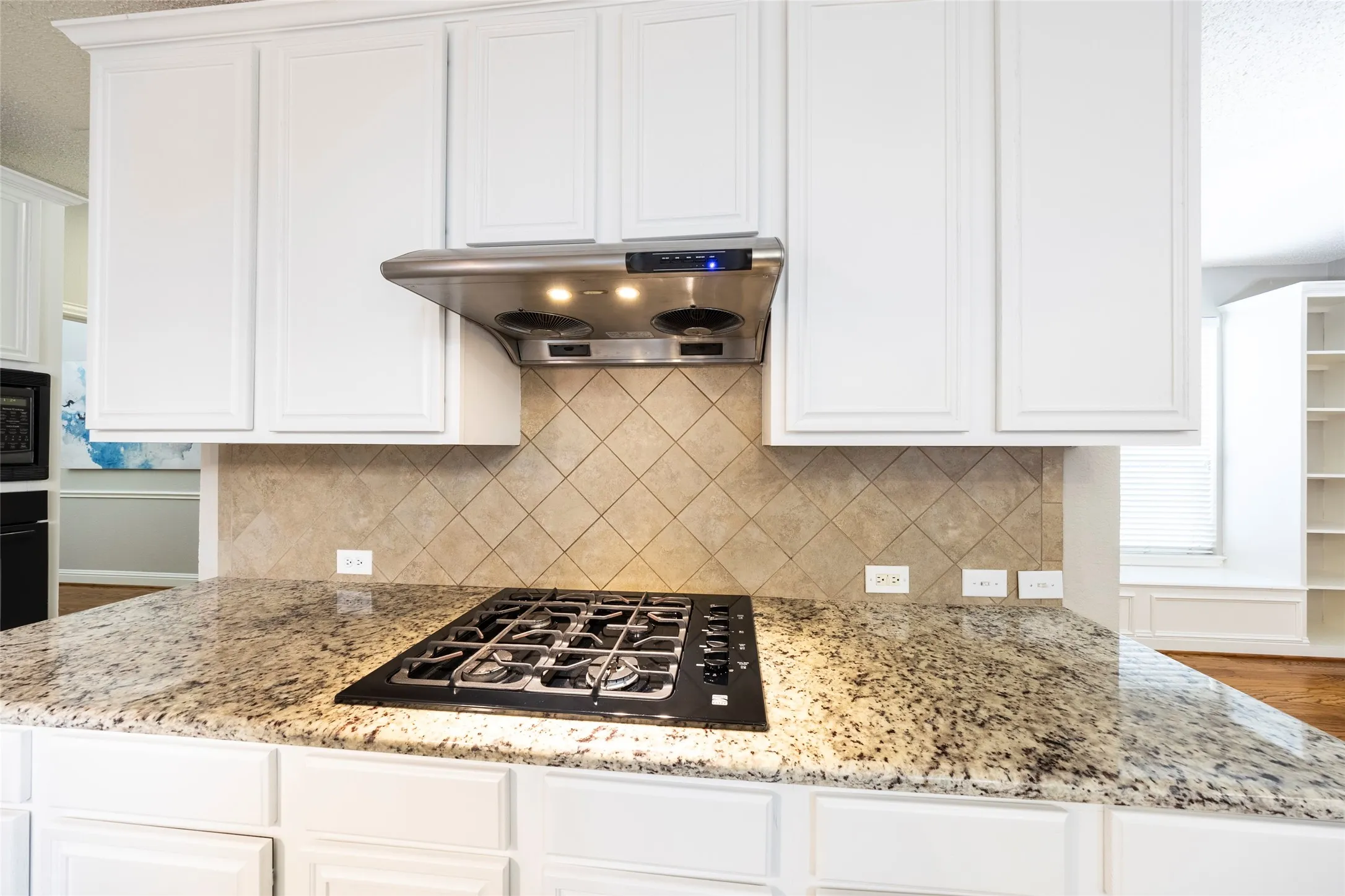 The kitchen features white cabinetry, a stainless steel range hood, a tiled backsplash, and granite countertops with an integrated gas cooktop