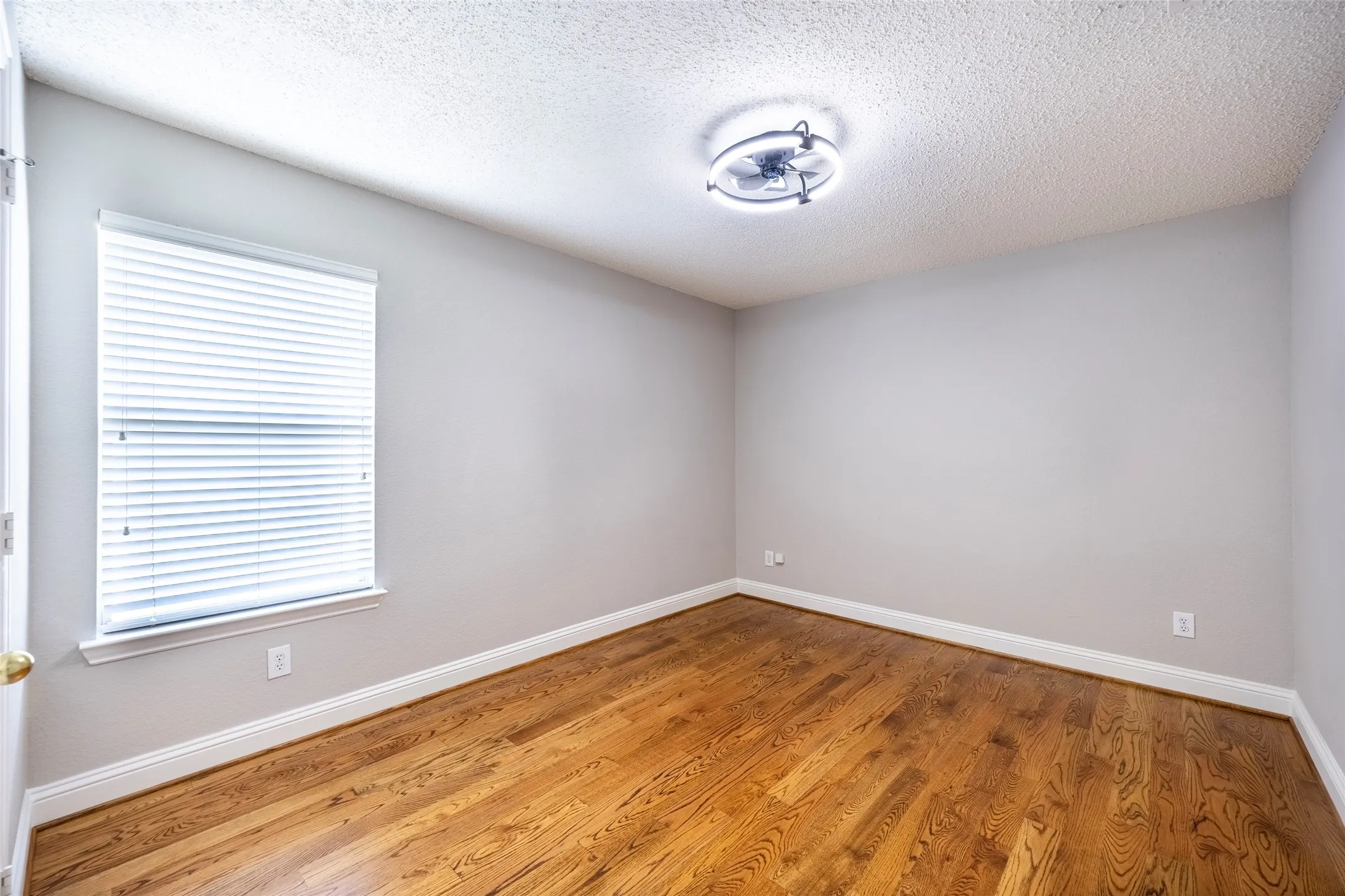 Room featuring hardwood floors, a window with blinds, and an overhead light fixture
